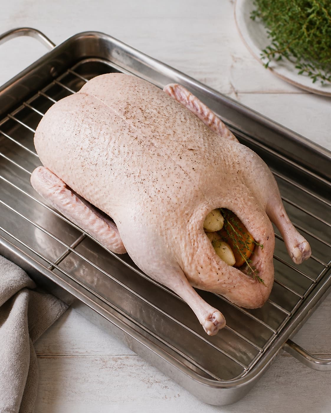 A single raw whole duck loosely filled with apple orange and thyme, seasoned and breast-up on a roasting rack over water, no browned skin under tilberedningen af andesteg langtidsstegt
