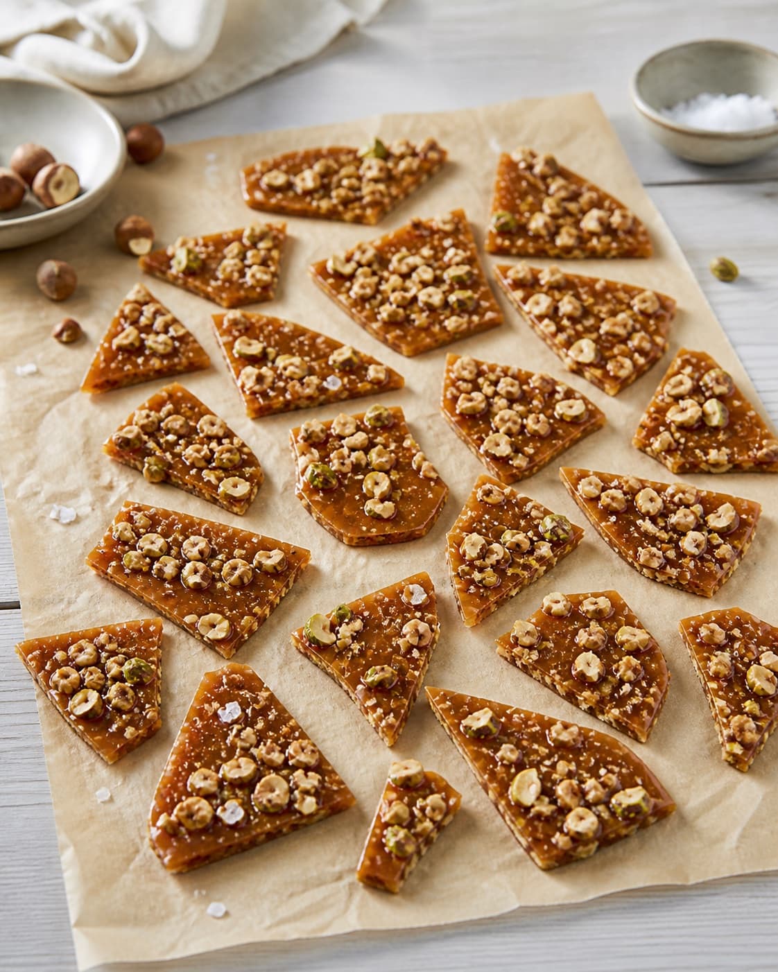 About twenty-four irregular crisp caramel shards with embedded hazelnuts pistachios and flaky salt, fully cooled and no unbroken slab under tilberedningen af karamelbrud