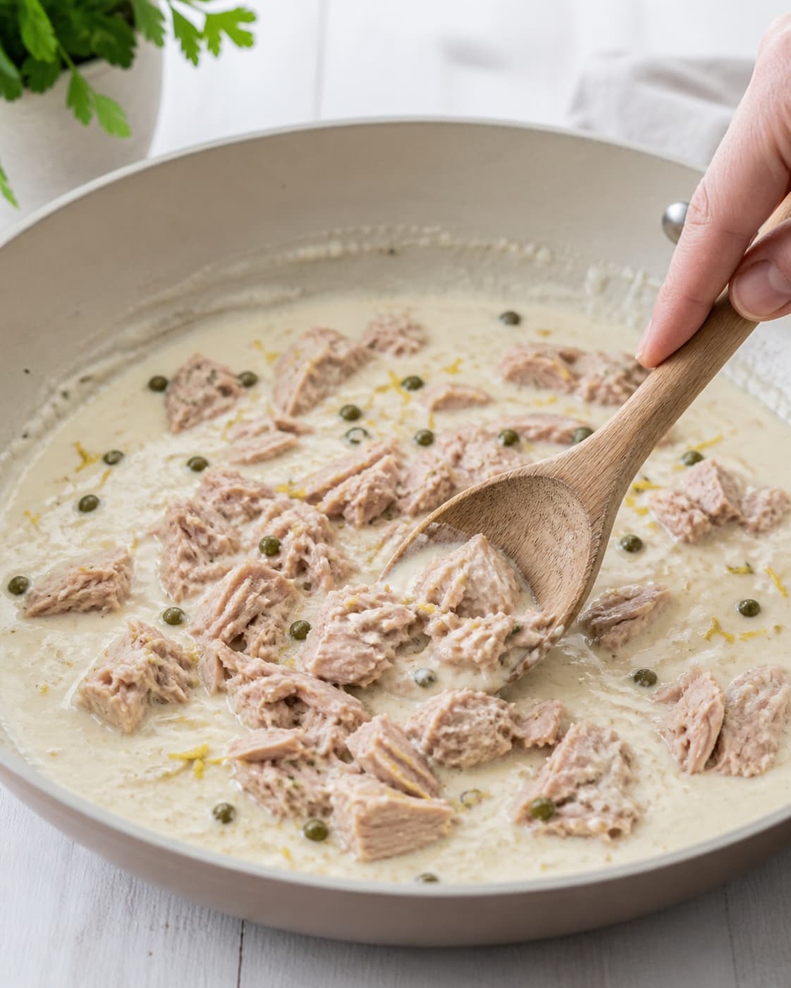 Creme fraiche capers lemon zest and pasta water forming a pale glossy sauce as large tuna flakes are gently folded in, no pasta yet under tilberedningen af pasta med tunsauce
