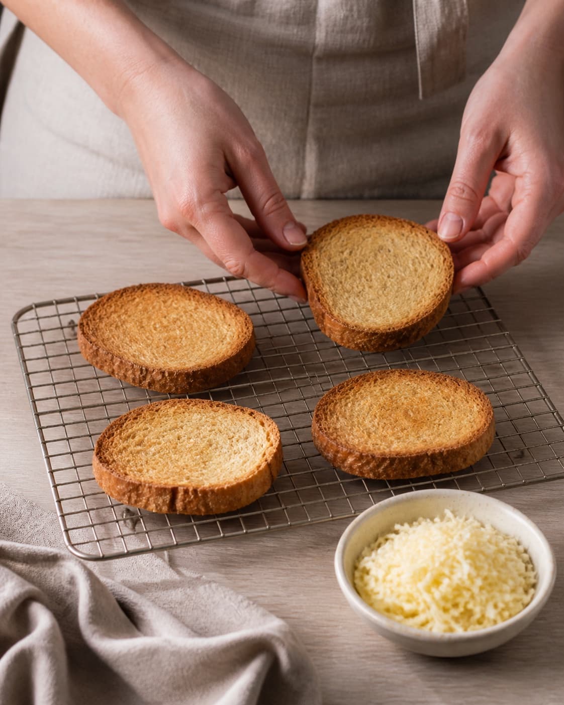 Exactly four toasted bread slices fully visible beside one bowl of grated Gruyere, no soup bowls and no melted cheese under tilberedningen af løgsuppe