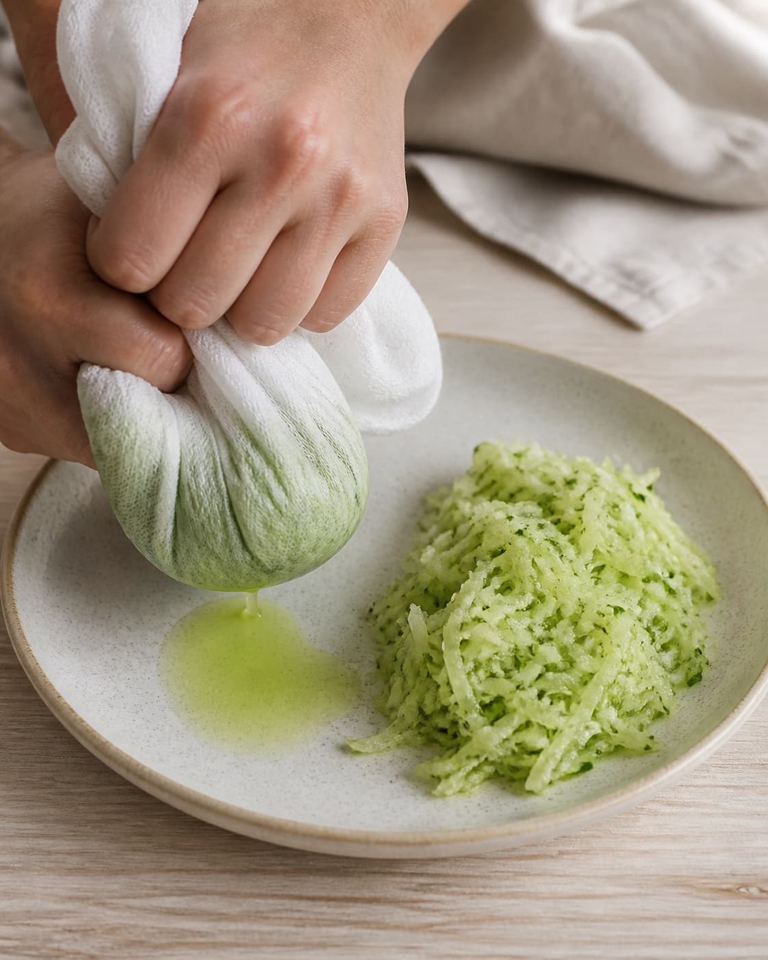 Grated salted cucumber being firmly squeezed in one clean cloth, dry separated shreds beside it, no yoghurt or herbs under tilberedningen af raita