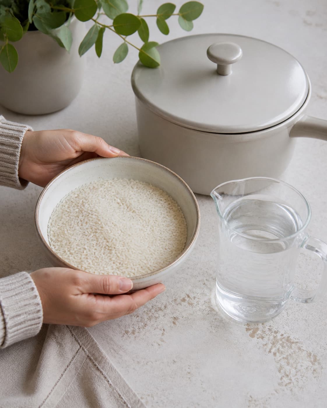Dry white basmati rice in one measured bowl beside one measured jug of clear water and an empty lidded saucepan, no cooked rice under tilberedningen af ris – kogetid