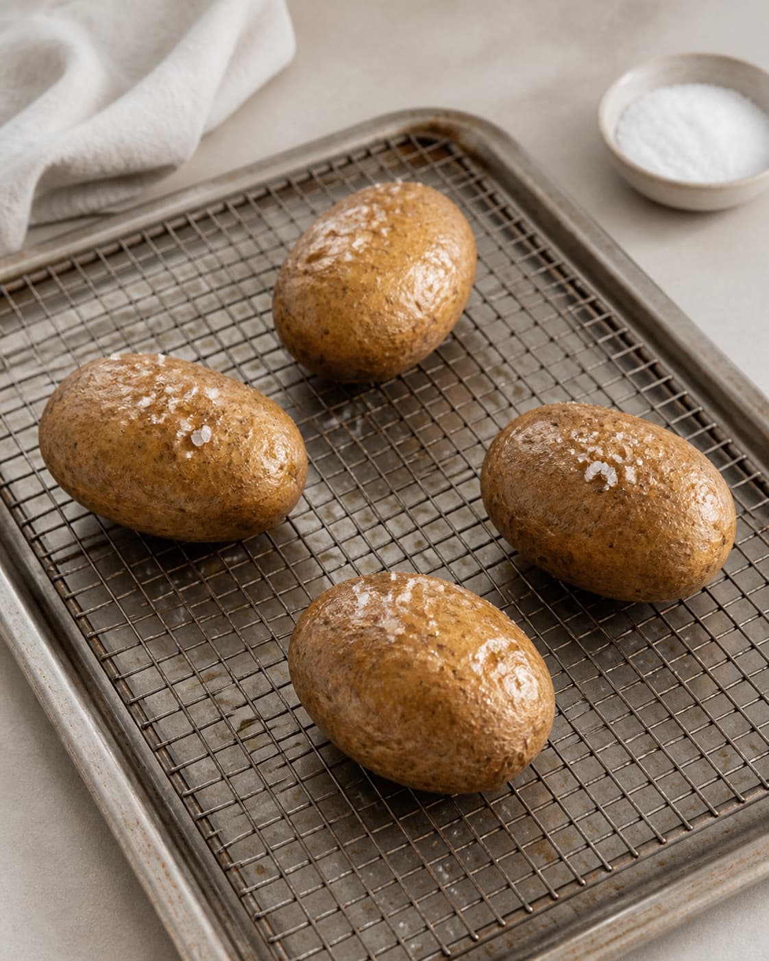 Exactly four whole raw potatoes coated lightly with oil and coarse salt, spaced apart on one wire rack, no butter or cut potatoes under tilberedningen af bagte kartofler
