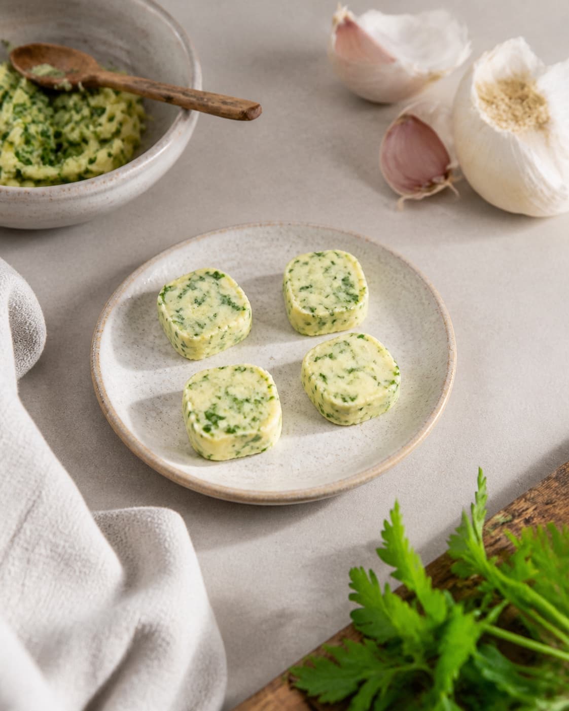 Exactly four equal portions of firm parsley garlic butter with fine green flecks on one small plate, no potatoes bread or melted butter under tilberedningen af bagte kartofler
