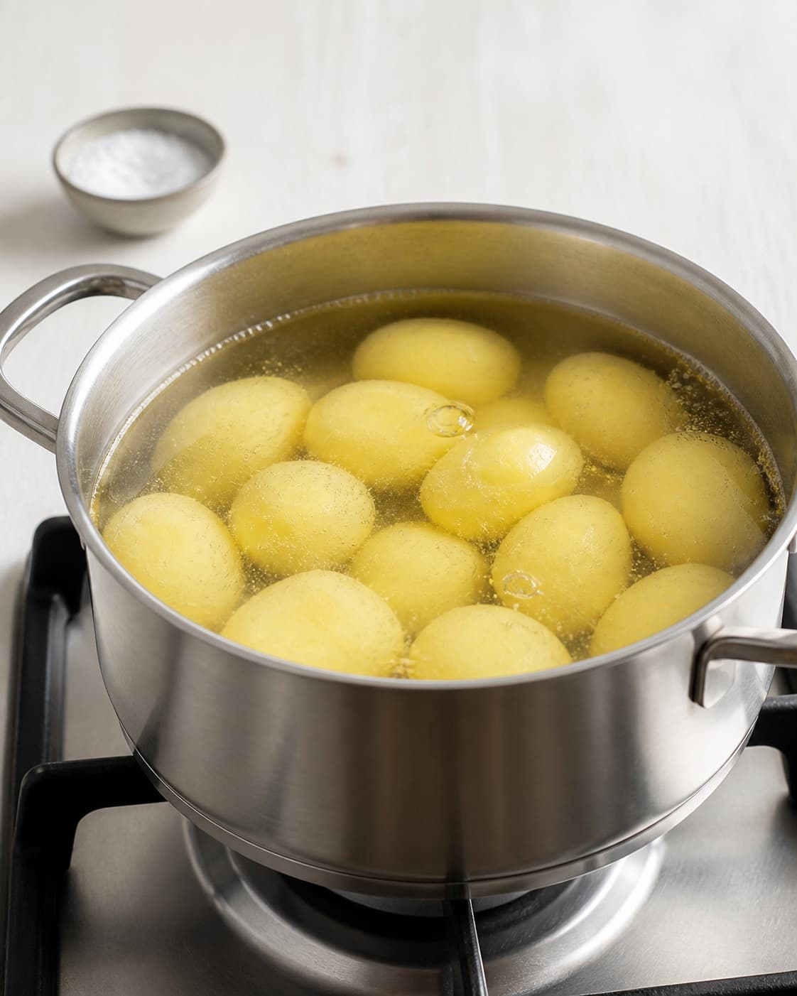 Peeled potatoes just covered with cold salted water in one saucepan reaching the first gentle bubbles, no garnish or cooked potatoes under tilberedningen af kogte kartofler