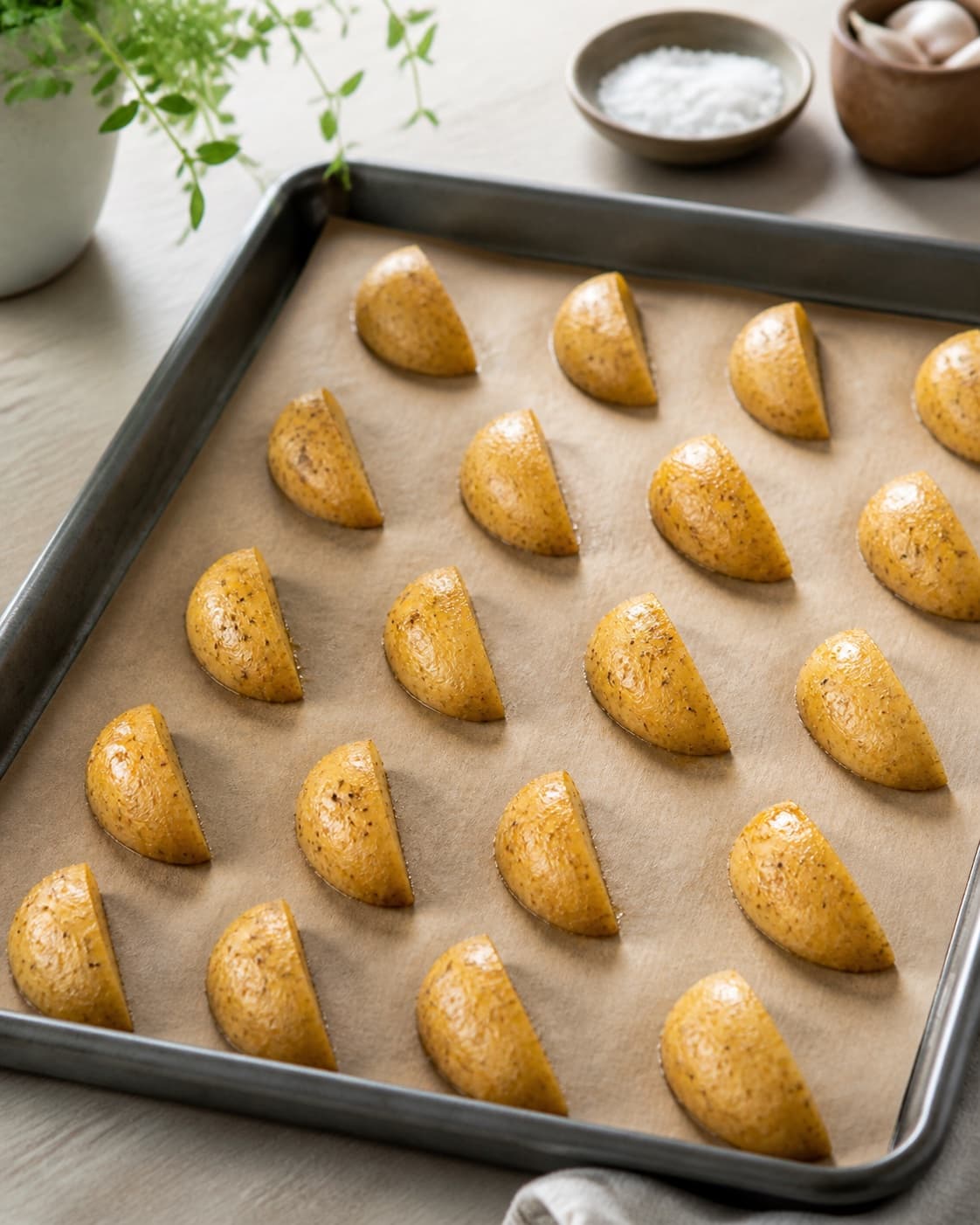 Seasoned raw potato wedges arranged in one uncrowded single layer on a hot tray, cut sides down with clear gaps, no stacked pieces under tilberedningen af kartoffelbåde i ovn