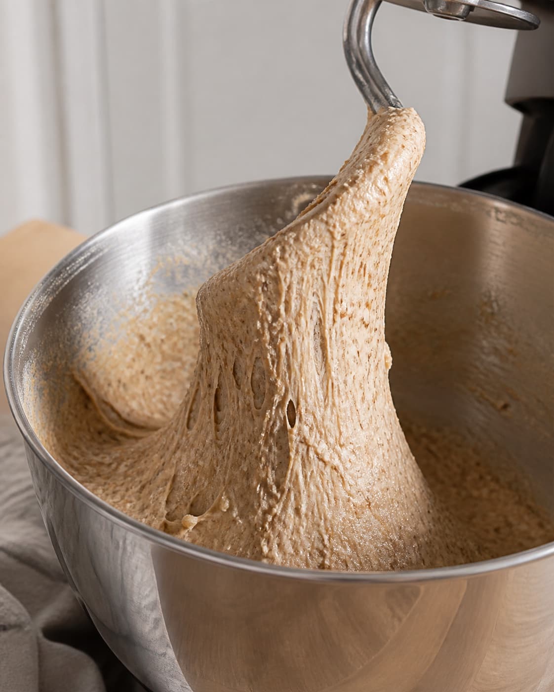 Sticky rye dough stretching from one dough hook with visible grains and slight sheen, no proofed dough shaped rolls or oats under tilberedningen af rugboller