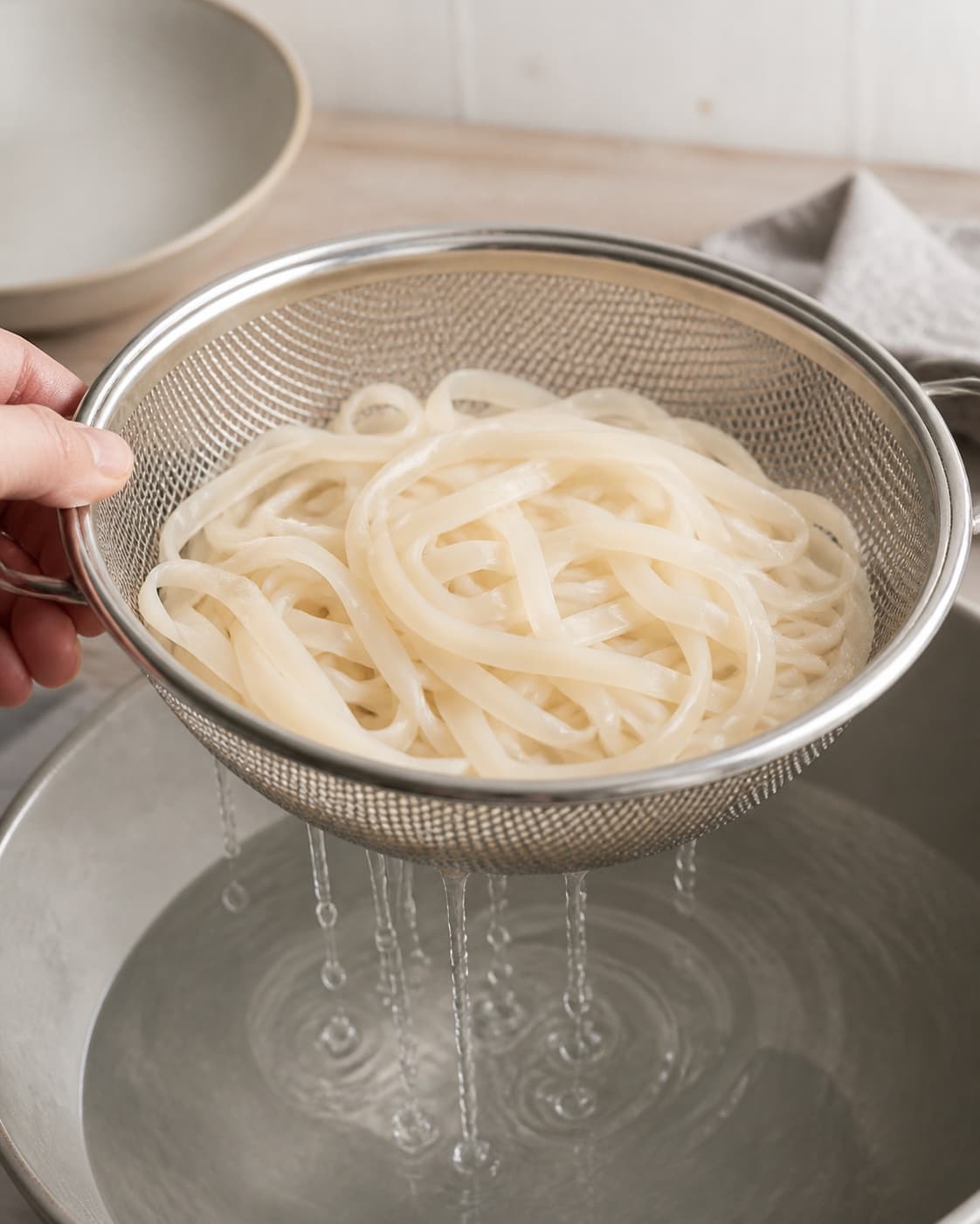 Pale wide rice noodles soaking then draining in one colander while still flexible but firm, no sauce meat eggs or vegetables under tilberedningen af pad thai