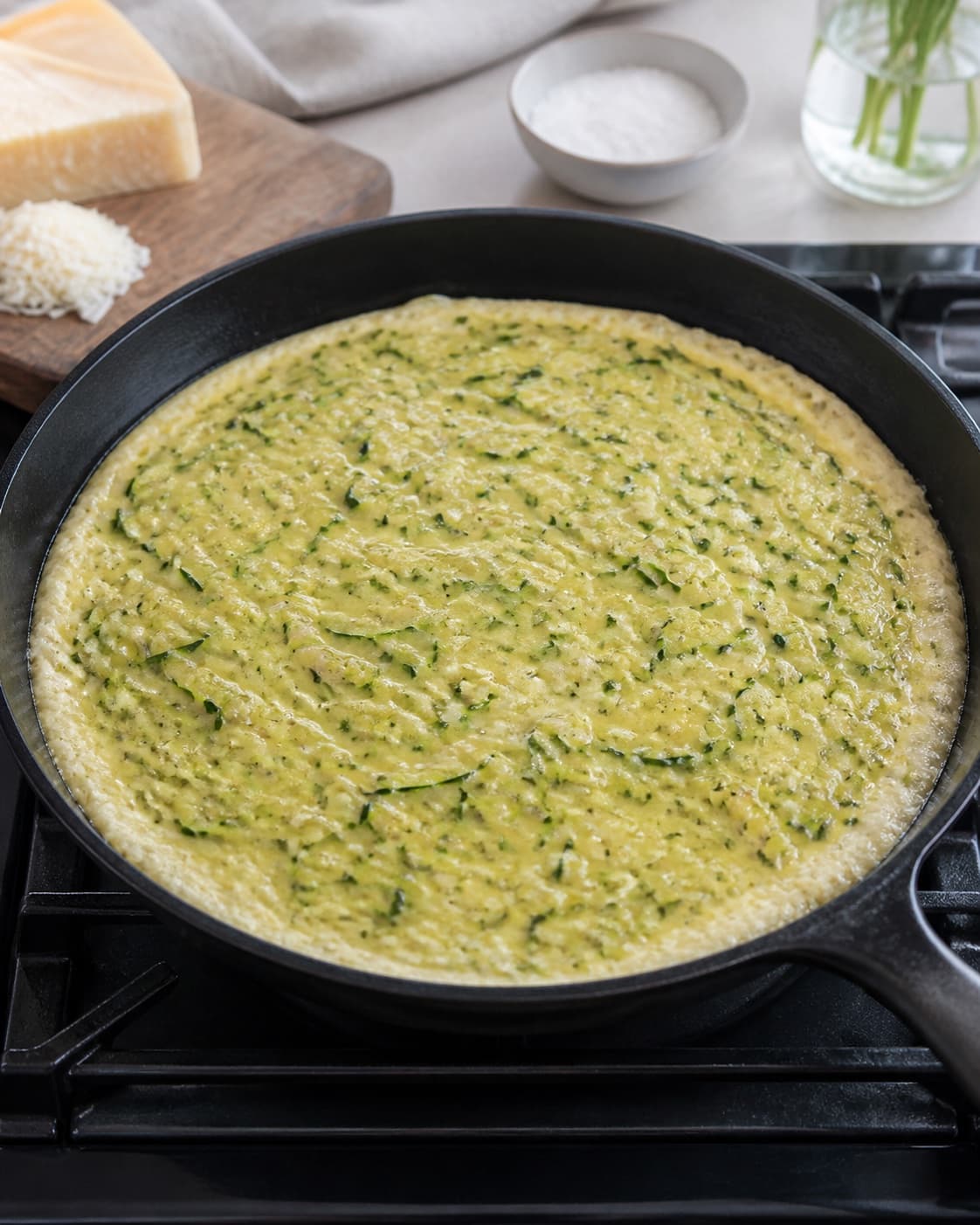 One ovenproof skillet of zucchini frittata with set pale edges and a clearly soft glossy unset centre, no browned top salad or serving plate under tilberedningen af frittata med squash
