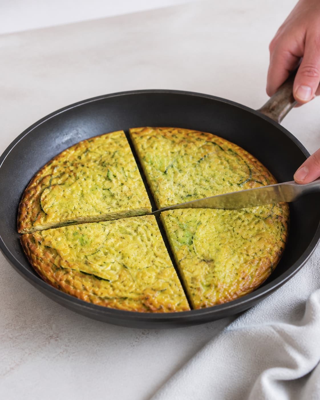 One golden zucchini frittata in its skillet cut into exactly four equal wedges, moist green-flecked crumb, no raw liquid egg salad or extra food under tilberedningen af frittata med squash