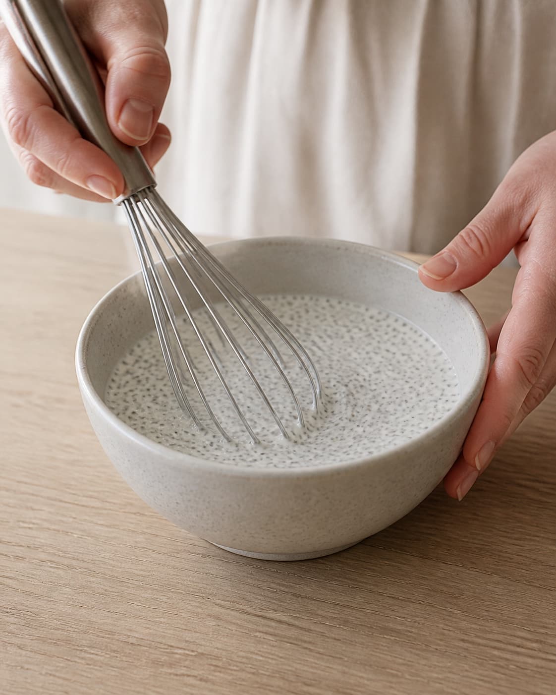 White coconut mixture with evenly dispersed black chia seeds being whisked in one bowl, no yoghurt berries nuts honey or finished porridge under tilberedningen af kokos-chiagrød