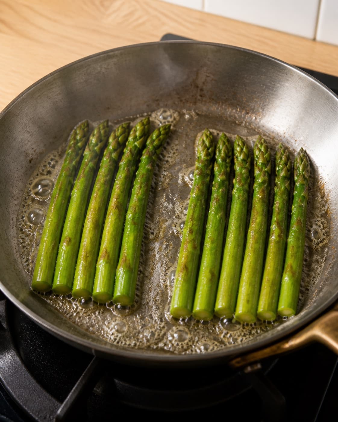 Exactly twelve whole green asparagus spears flash-searing in butter in one skillet with light brown marks, no white asparagus sauce roe or plated food under tilberedningen af asparges med ramsløg og stenbiderrogn