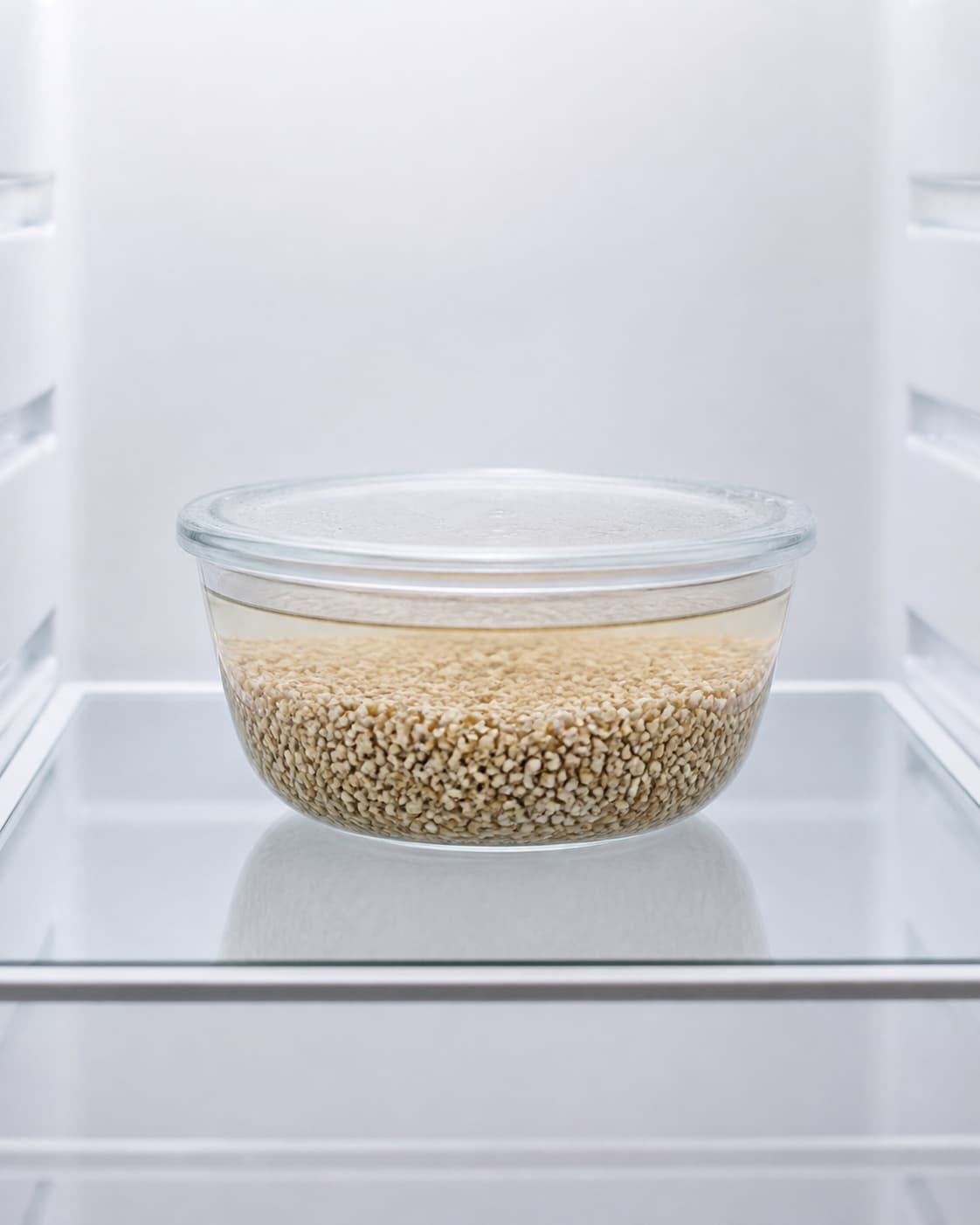 One covered clear bowl of whole buckwheat groats submerged in clear water alone on a refrigerator shelf, no milk spices banana nuts or finished porridge under tilberedningen af boghvedegrød med karamelliseret banan