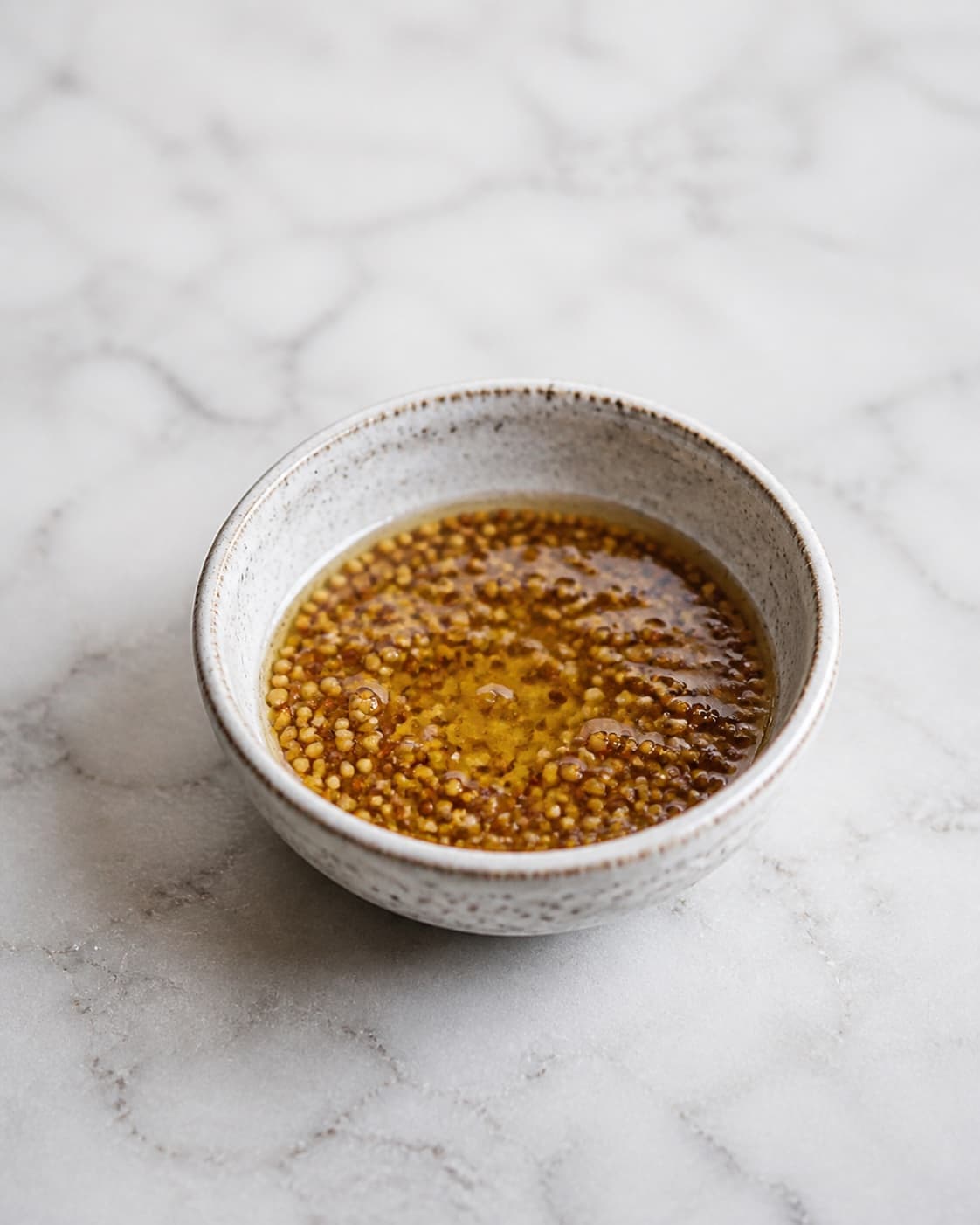 One small bowl of glossy golden vinaigrette with visible whole mustard grains, no greens orange segments nuts or serving platter under tilberedningen af blodappelsinsalat med rucola