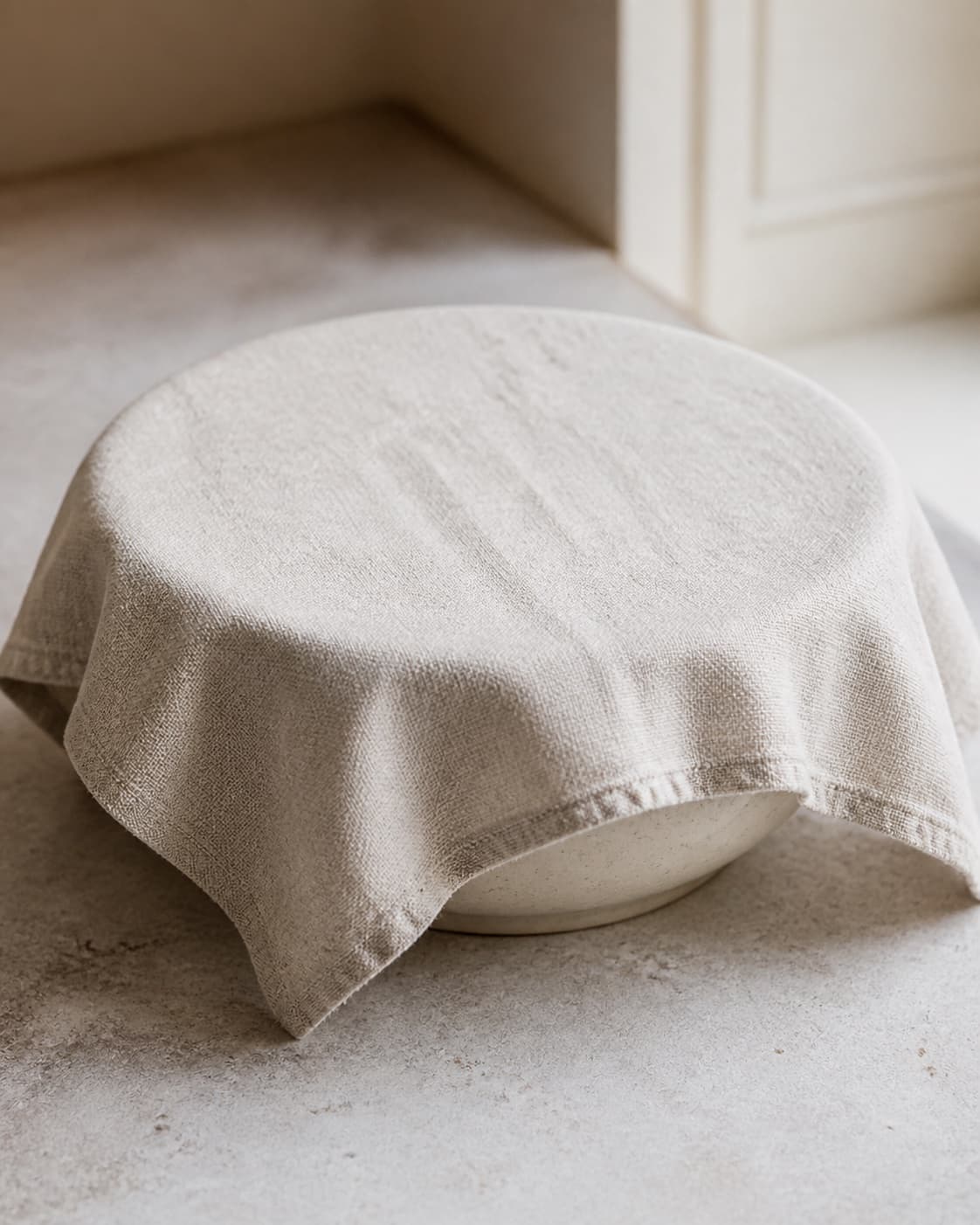 One large bowl of risen rye dough covered by one clean cloth on a kitchen counter, no baking tray butter or finished breads under tilberedningen af chokorug
