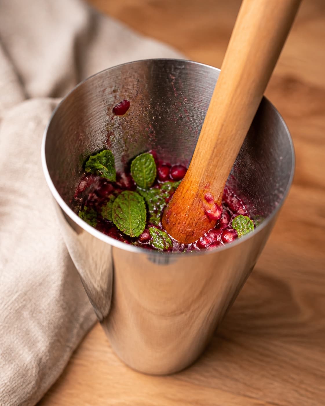 One open cocktail shaker holding muddled ruby pomegranate arils fresh mint leaves and honey, no ice alcohol soda lime or glasses under tilberedningen af nytårscocktail med granatæble og snaps