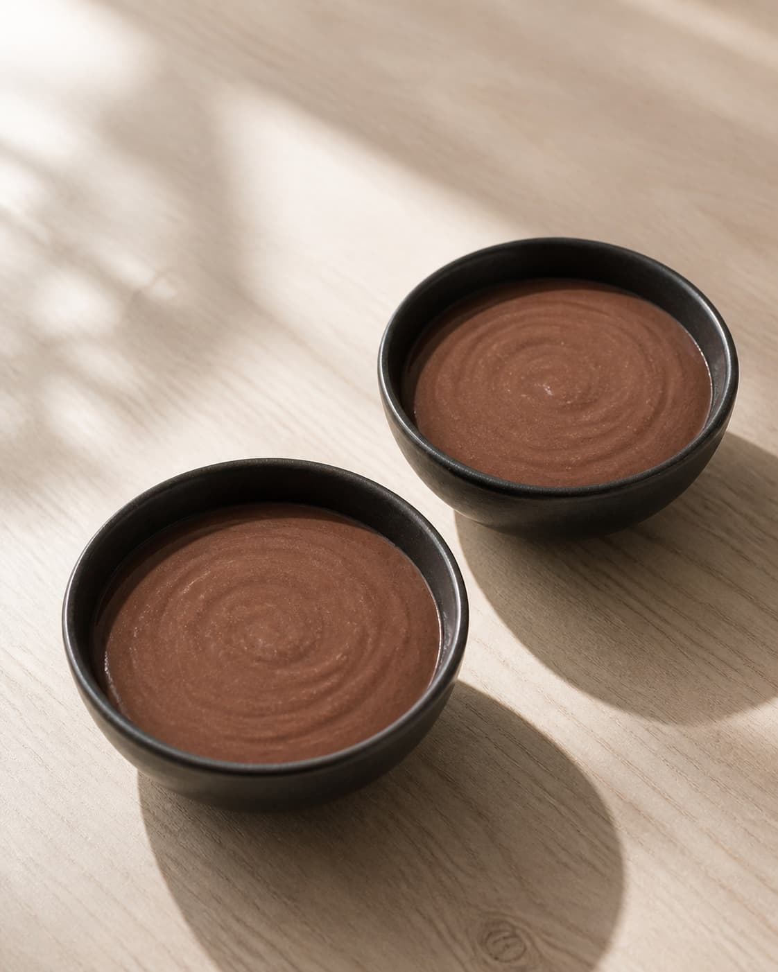 Exactly two low bowls holding equal portions of smooth dark cocoa smoothie, plain surface with no fruit nuts seeds garnish or extra bowls under tilberedningen af kakaobowl