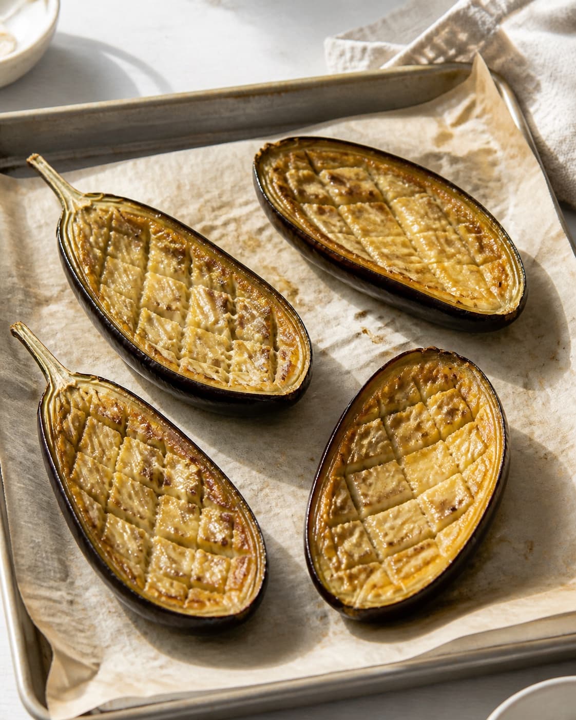 Exactly four baked aubergine halves with golden collapsed tender scored flesh on one tray, no bulgur yogurt pomegranate or herbs under tilberedningen af bagte auberginer med bulgur