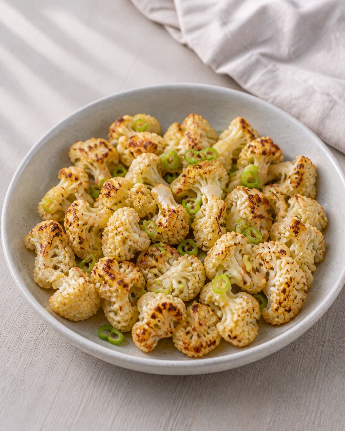 One serving platter of golden pan-seared cauliflower evenly scattered with chopped spring onion, no tahini pomegranate or other herbs under tilberedningen af stegt blomkål med tahin og granatæble