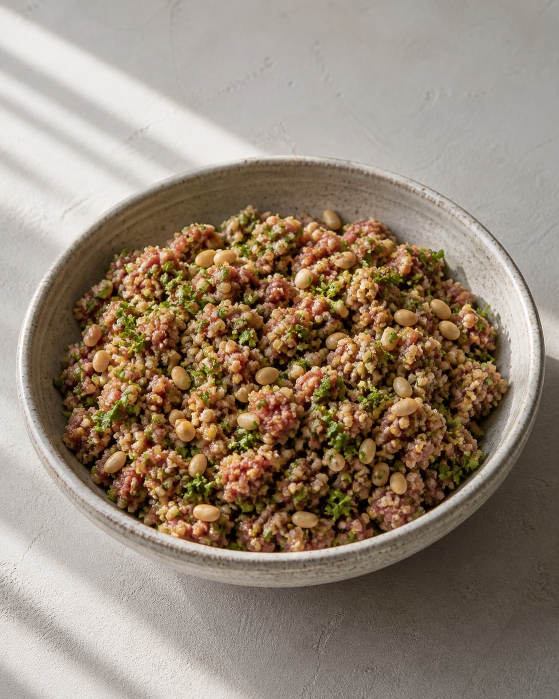 One bowl of uniform raw minced-lamb filling visibly mixed with bulgur, parsley and toasted pine nuts, no squash dressing or pomegranate under tilberedningen af farserede squash med bulgur