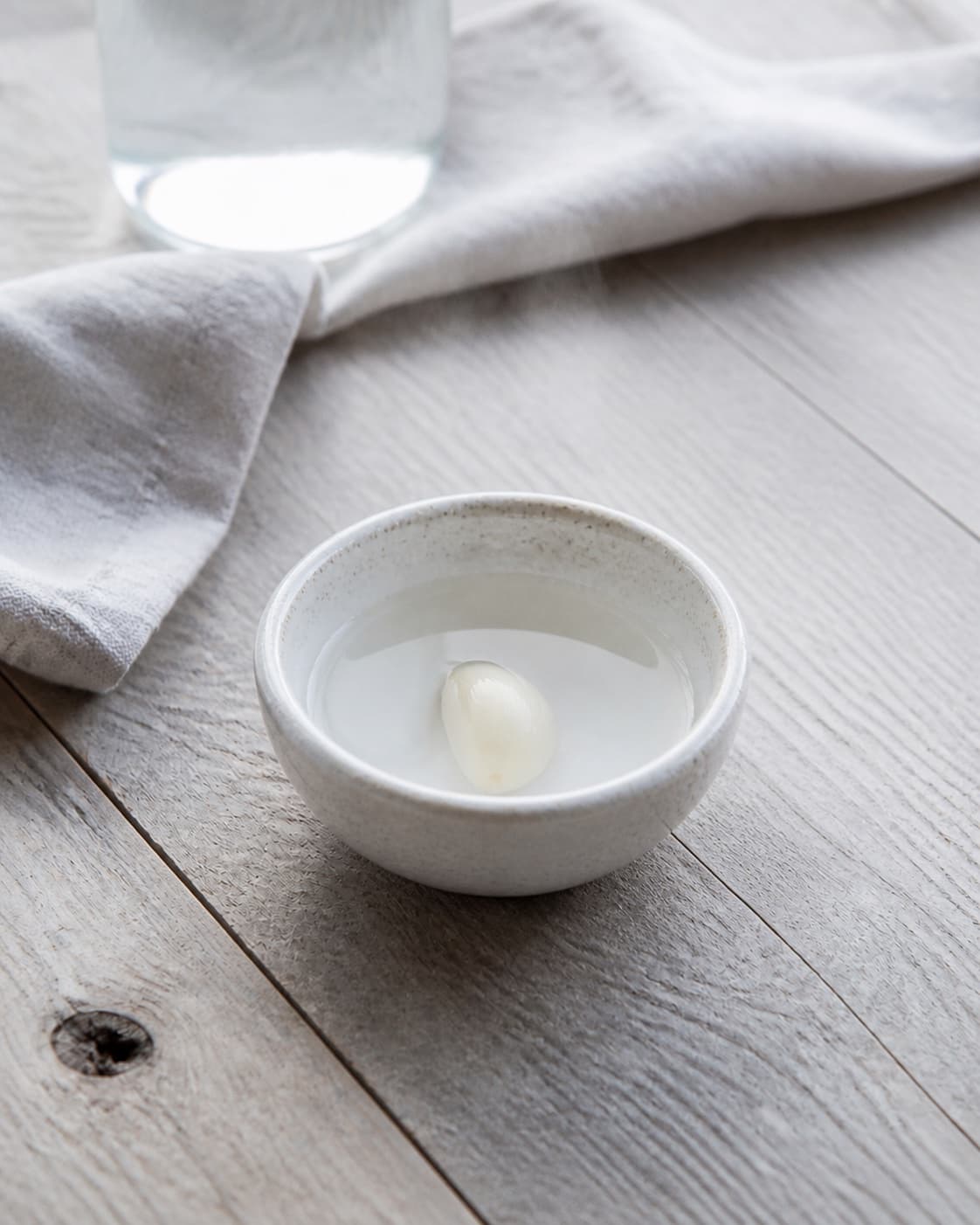 One small bowl holding one peeled garlic clove submerged in hot water, no sesame seeds dressing blender or extra ingredients under tilberedningen af goma dressing