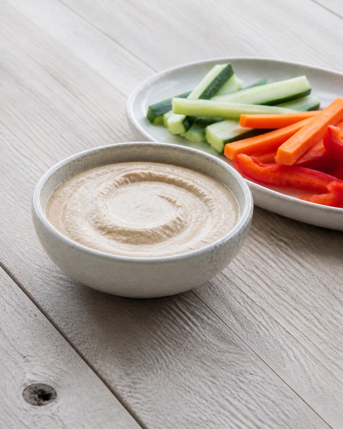 One small serving bowl of smooth pale-brown goma dressing beside simple vegetable sticks, no extra bowls jars or garnish under tilberedningen af goma dressing