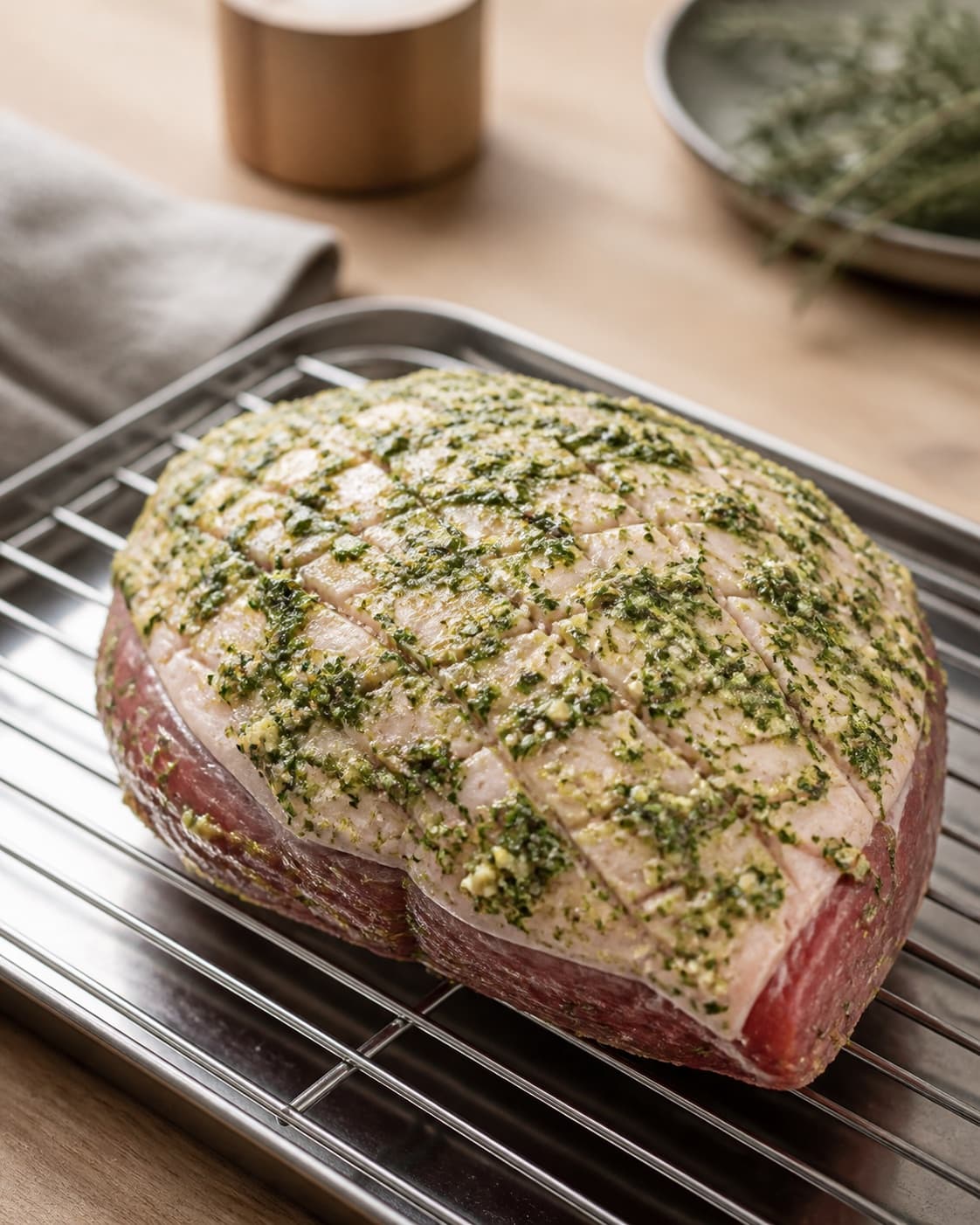One raw lamb rump evenly coated with green herb-garlic paste worked into the scored fat cap on a rack, no sides under tilberedningen af lammeculotte