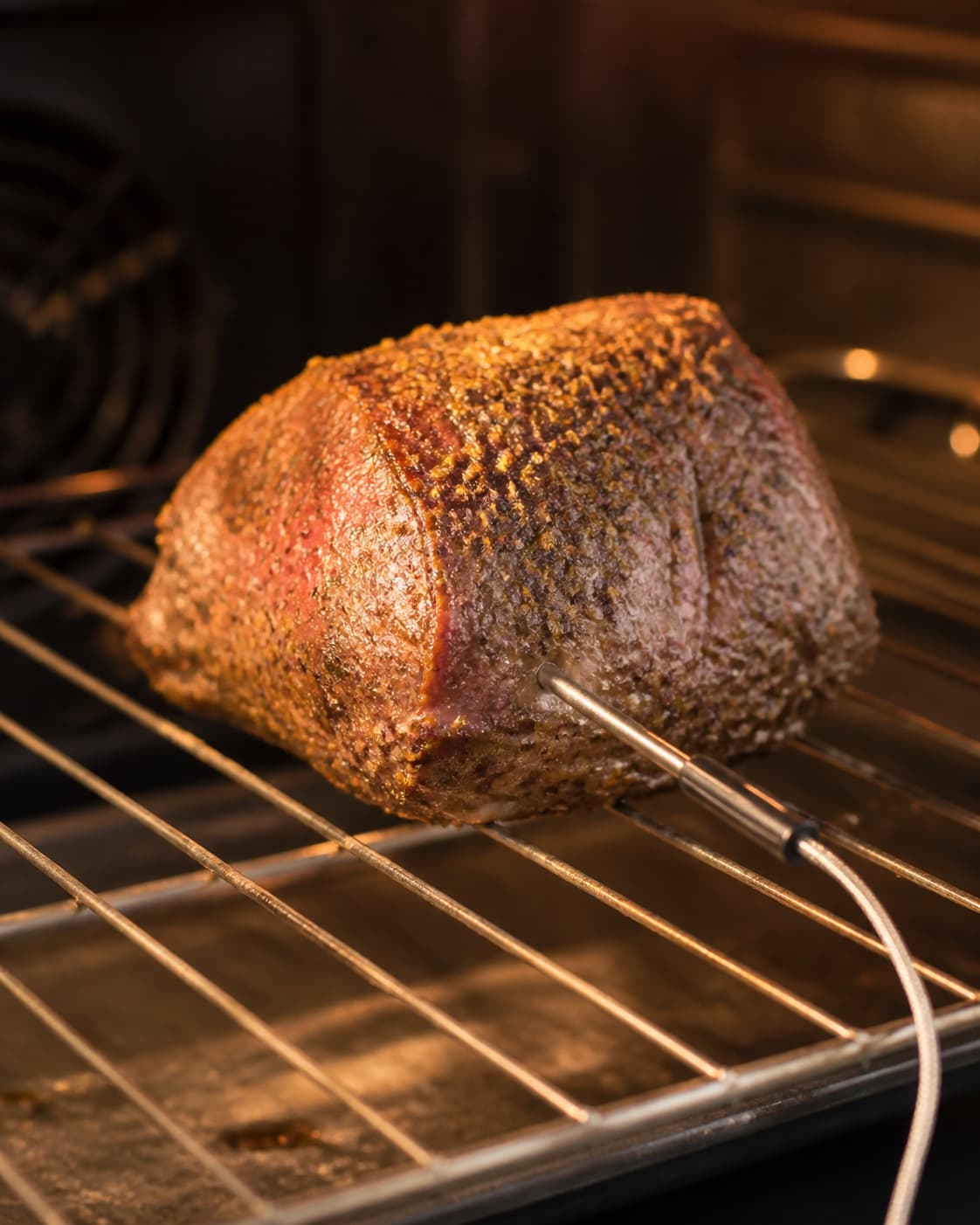 One herb-crusted lamb rump on an oven rack with a meat thermometer inserted into its centre, no slices sides or garnish under tilberedningen af lammeculotte