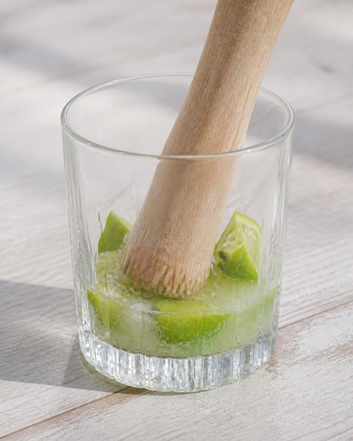 One sturdy cocktail glass holding muddled lime wedges, sugar and visible fresh lime juice at bottom, no alcohol ice or extra glass under tilberedningen af caipirinha cocktail