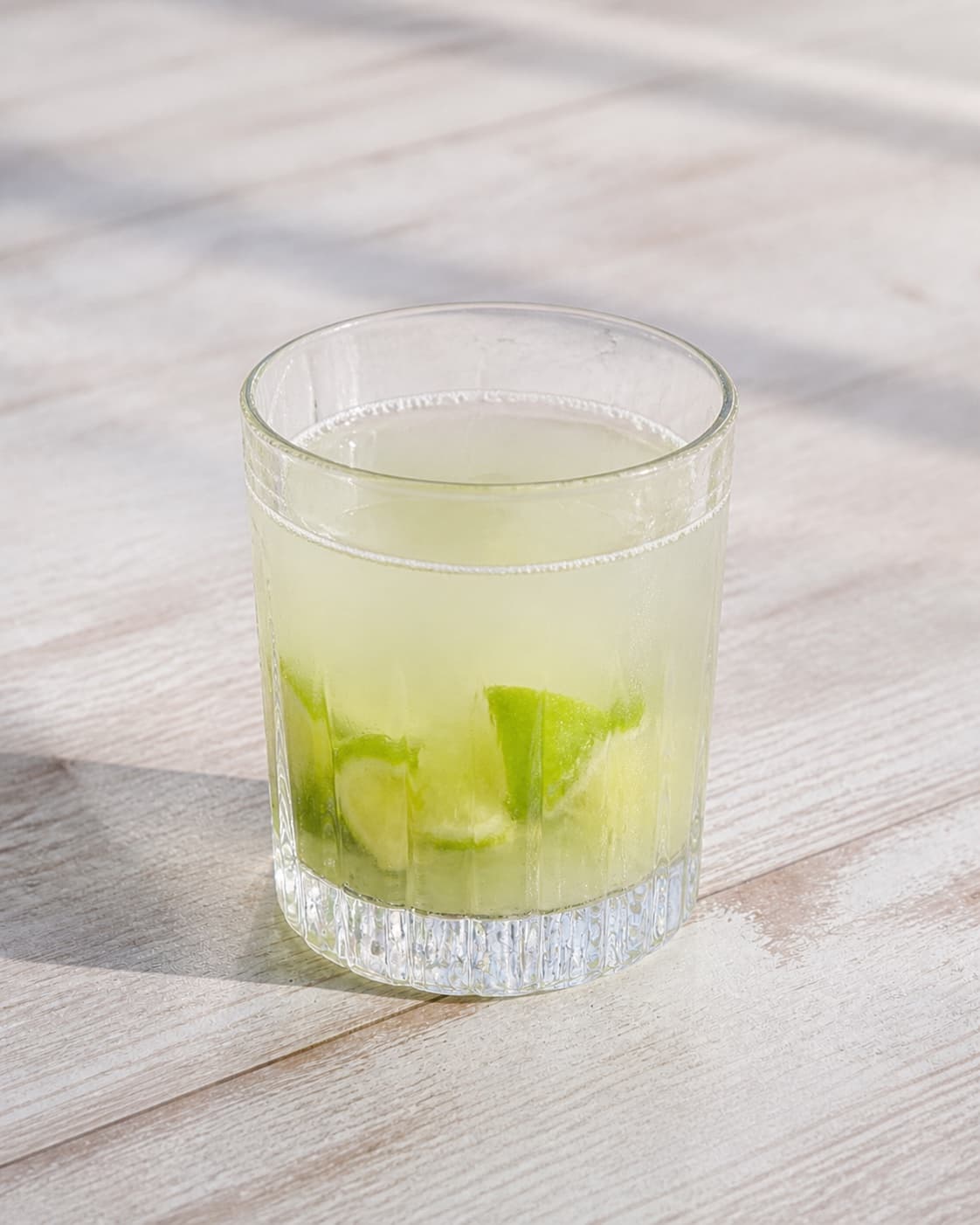 One cocktail glass with muddled lime, cachaca and clear syrup mixed together, no ice garnish bottle or extra glasses under tilberedningen af caipirinha cocktail