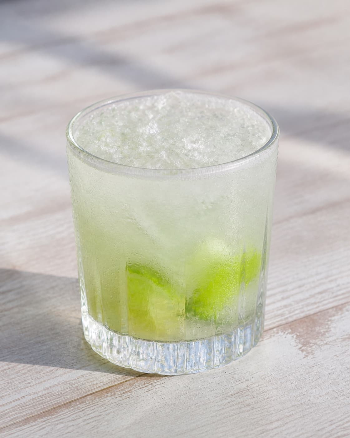 One finished single glass of caipirinha filled with crushed ice and lime wedges, no straw extra glasses bottles text or garnish under tilberedningen af caipirinha cocktail