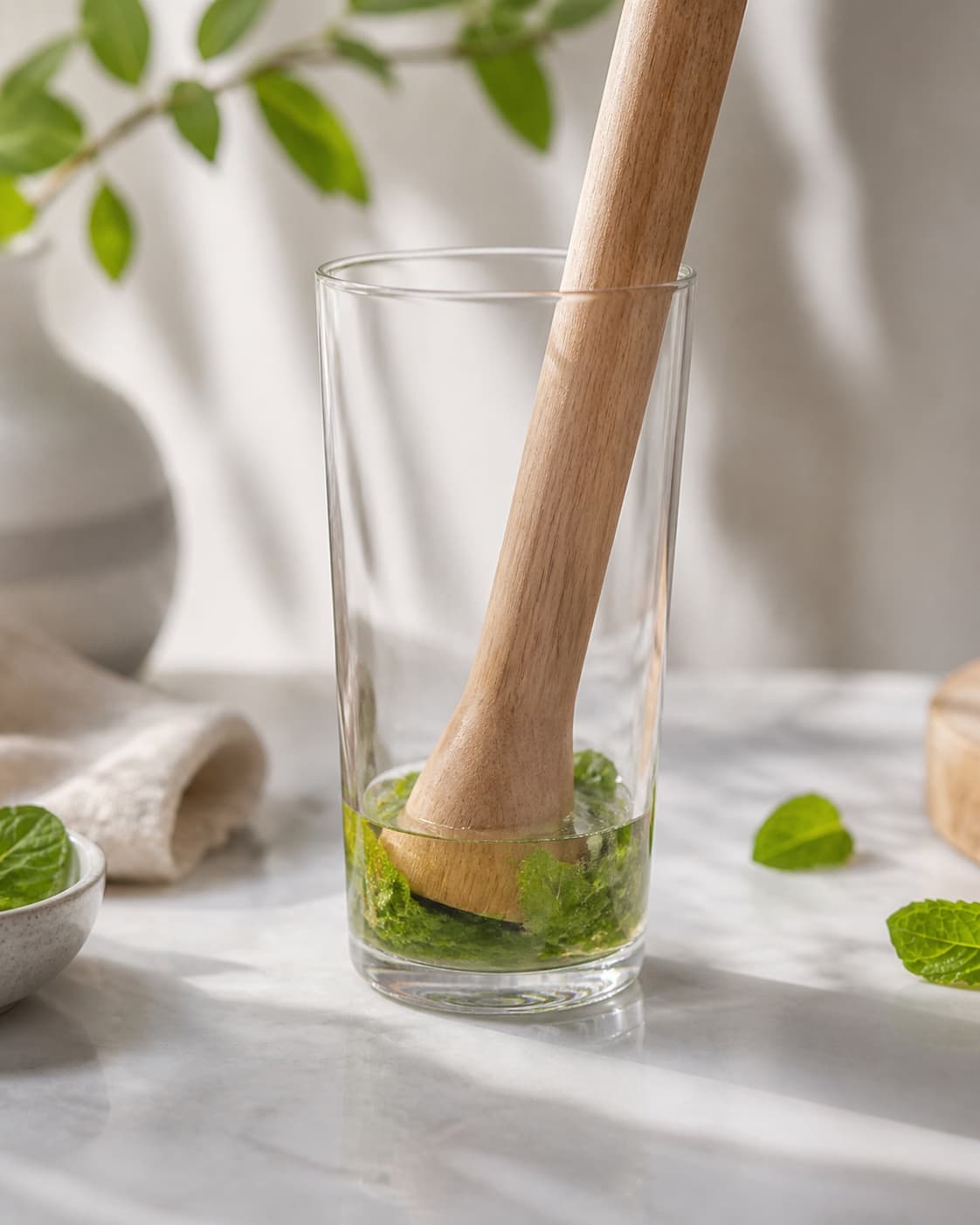 One tall cocktail glass containing lightly bruised green mint leaves in clear gin, no juice ice garnish bottle or extra glass under tilberedningen af summer breeze cocktail