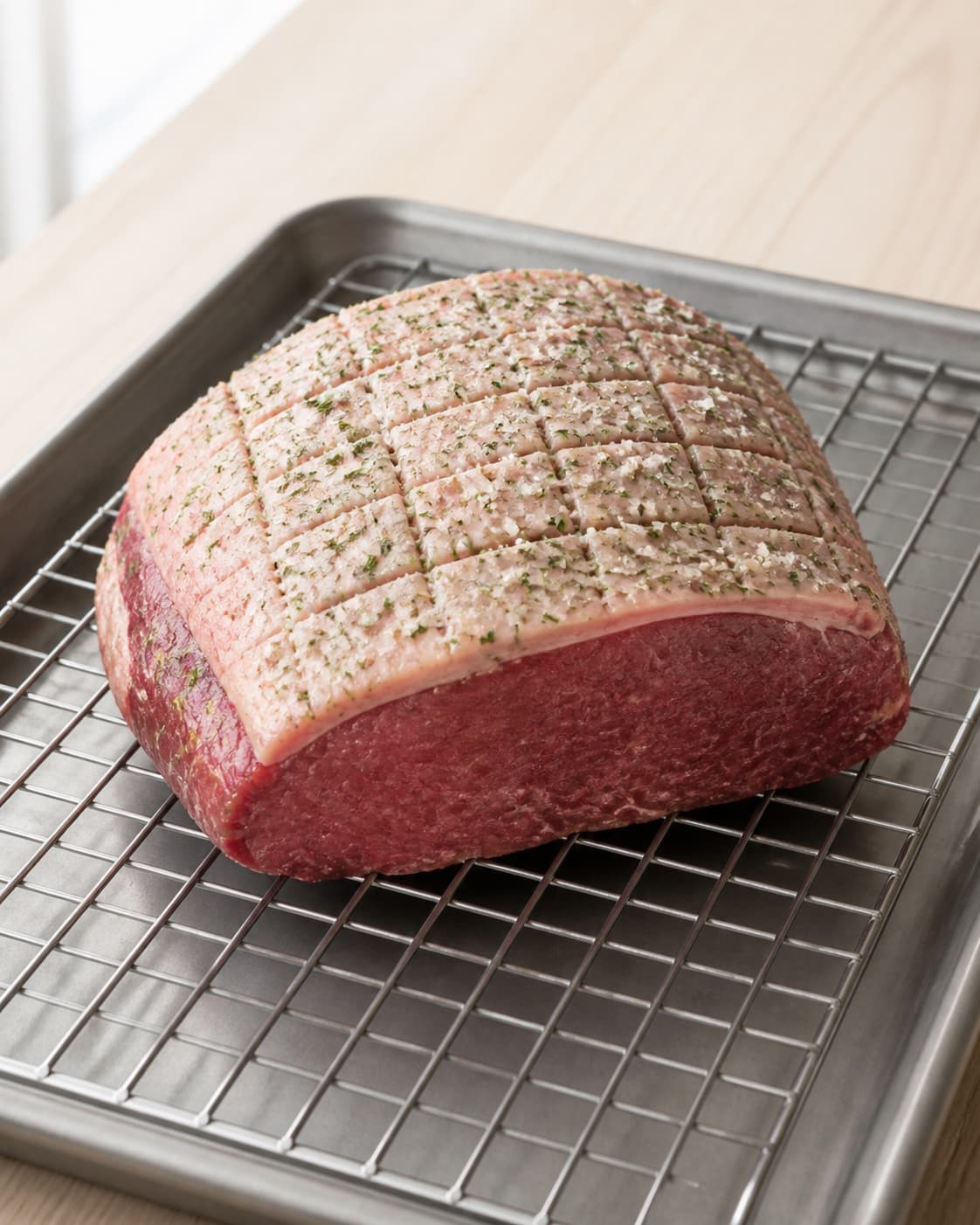 One raw beef rump cap on a rack with coarse green rosemary-garlic salt rubbed evenly into the scored fat cap, no side dishes under tilberedningen af culottesteg med rosmarin og hvidløg