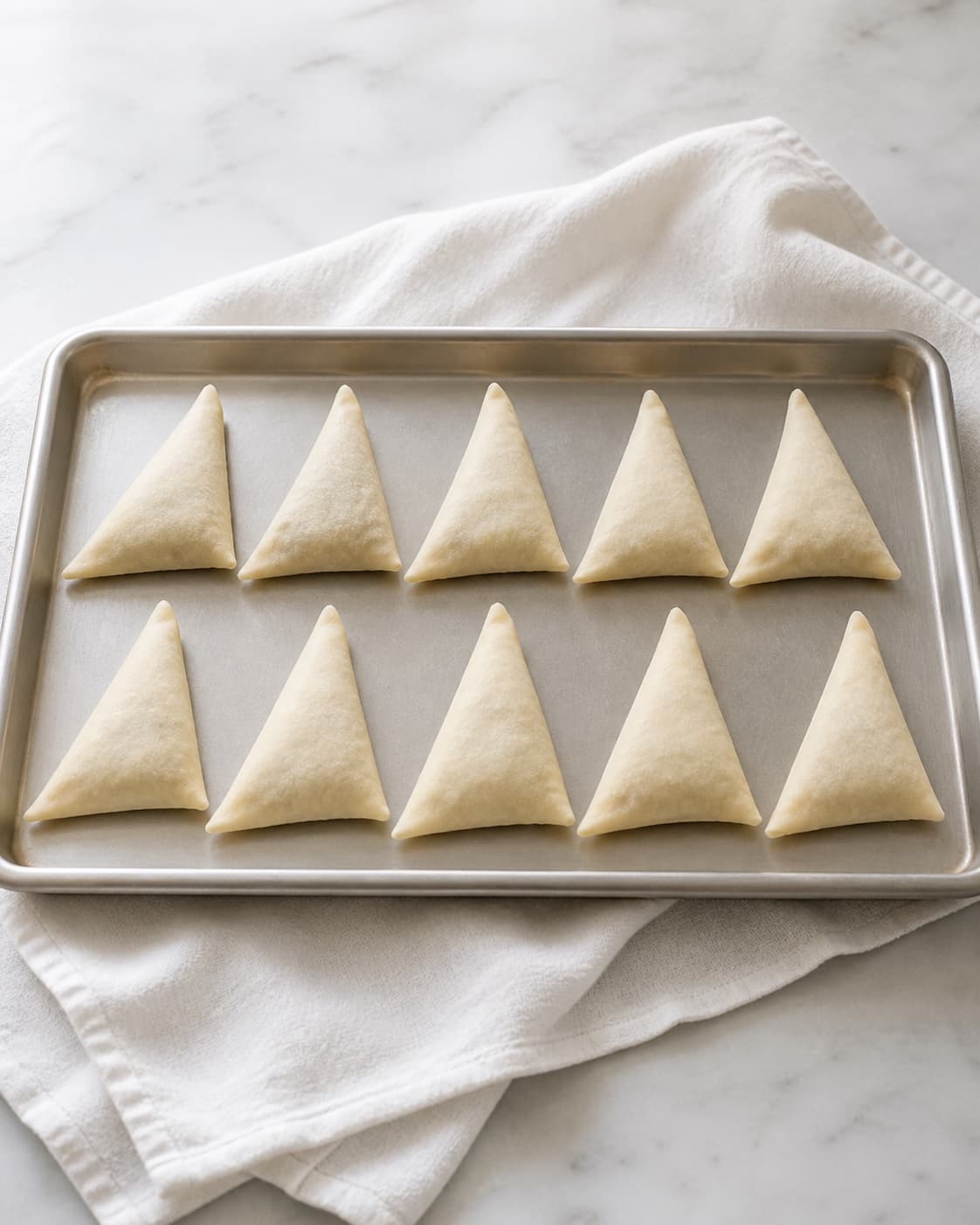 One baking tray holding exactly ten visible raw neatly sealed triangular wonton parcels, no fryer oil pot dip or garnish under tilberedningen af sprøde wontons