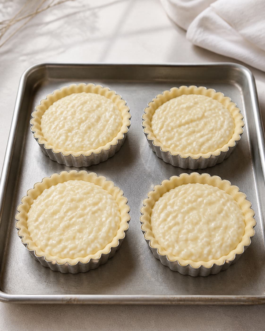 Exactly four small unbaked tart tins lined with thin pastry and evenly filled with creamy rice-vanilla filling, no sugar dusting garnish or extra tarts under tilberedningen af toscana ristærter