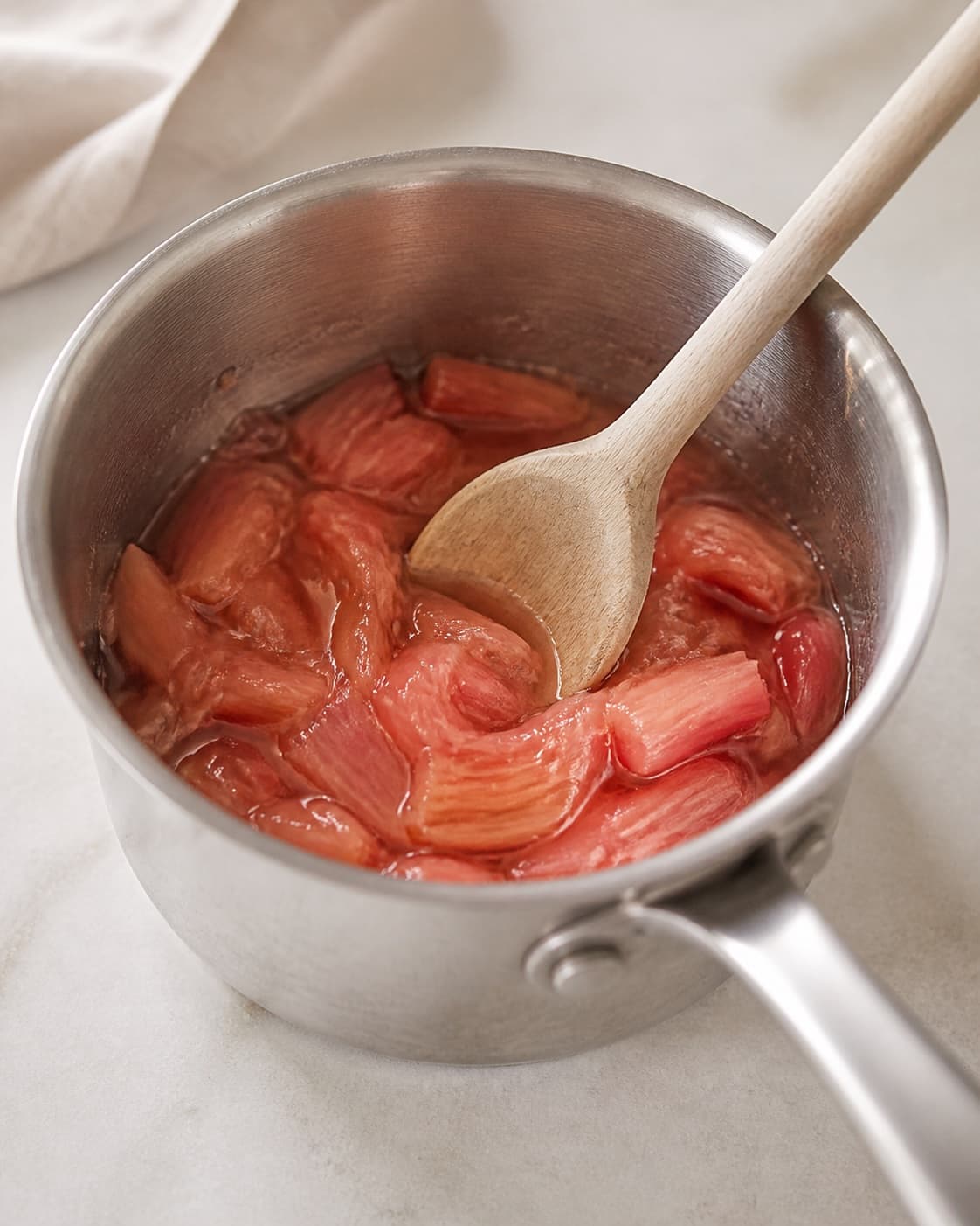One small saucepan holding softened collapsed pink rhubarb pieces in a little juice, no alcohol basil ice glasses or bottles under tilberedningen af rabarber-hyldeblomstcocktail med basilikum