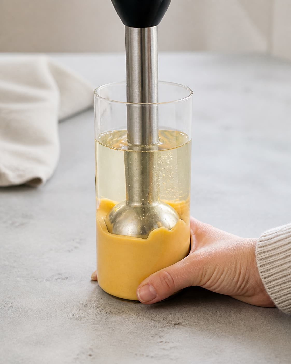 One narrow beaker with immersion blender held firmly at bottom and thick orange mayonnaise forming below a clear upper oil layer, no extra ingredients under tilberedningen af chilimayo