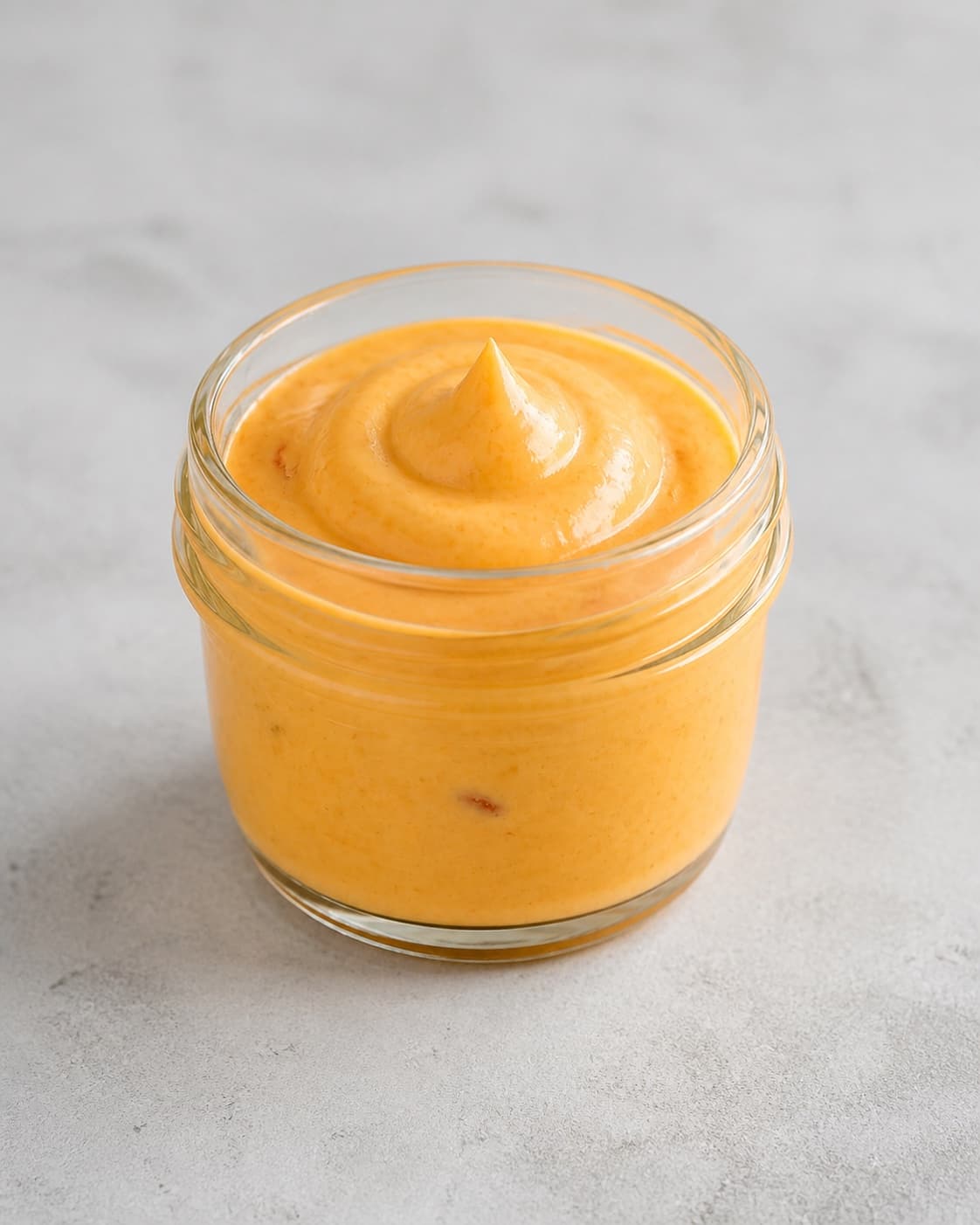 One clean open jar filled with thick orange chilli mayonnaise showing one soft peak, no fries burgers vegetables labels or extra dishes under tilberedningen af chilimayo