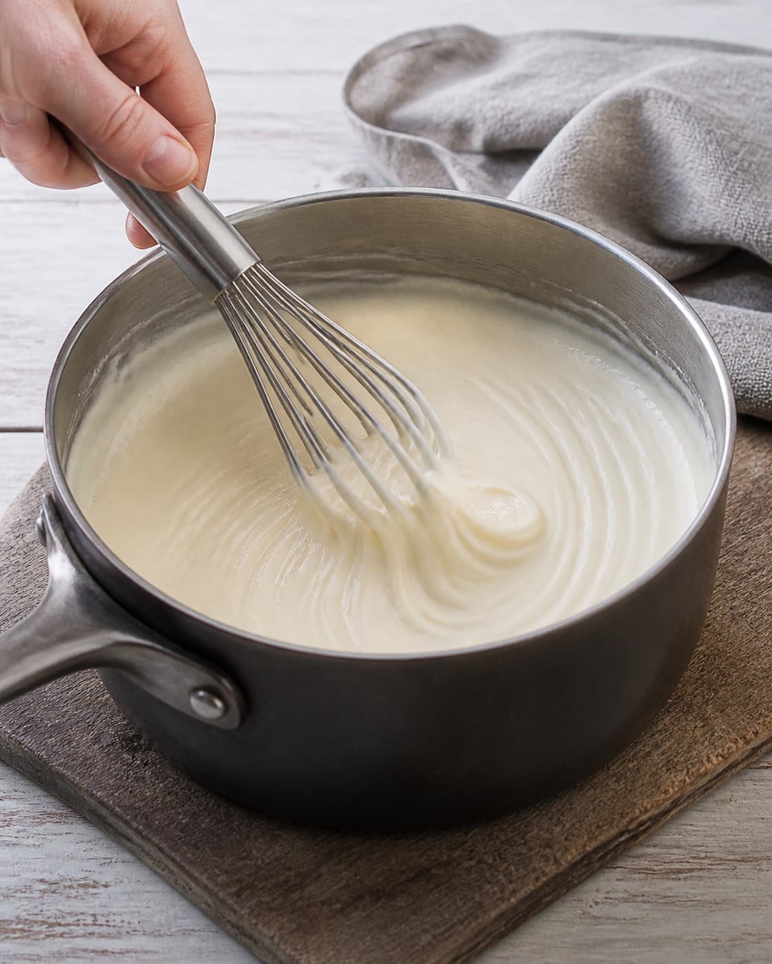 One small saucepan holding smooth thick white Mornay sauce that retains a clear whisk trail, no meat sauce vegetables baking dish or garnish under tilberedningen af moussaka med kartofler og aubergine