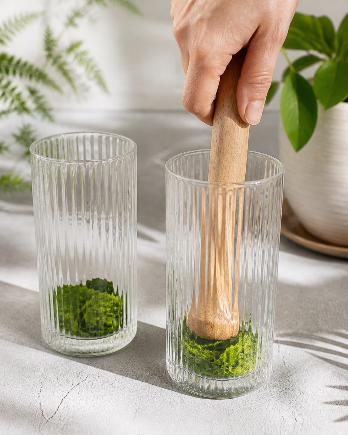 Exactly two empty tall glasses with lightly bruised green mint leaves at bottom and one muddler, no juice ice garnish or extra glasses under tilberedningen af ananasmojito med ingefær og mynte