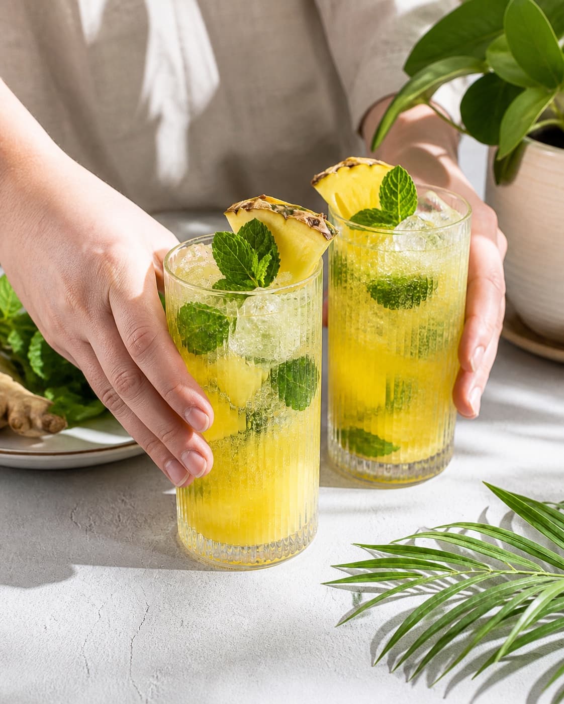 Exactly two finished tall yellow pineapple mojitos with fine bubbles, ice, mint and exactly one small pineapple wedge in each glass, no straws bottles text or extra glasses under tilberedningen af ananasmojito med ingefær og mynte