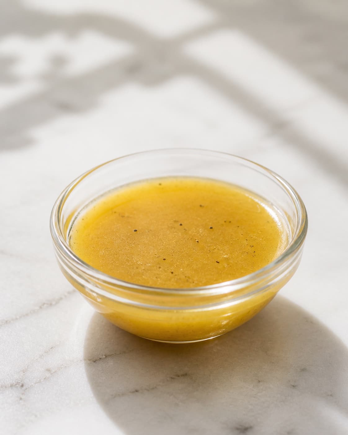 One small bowl of finished glossy golden vinaigrette with a few fine black pepper specks, no salad herbs bread or extra dishes under tilberedningen af vinaigrette dressing til salat