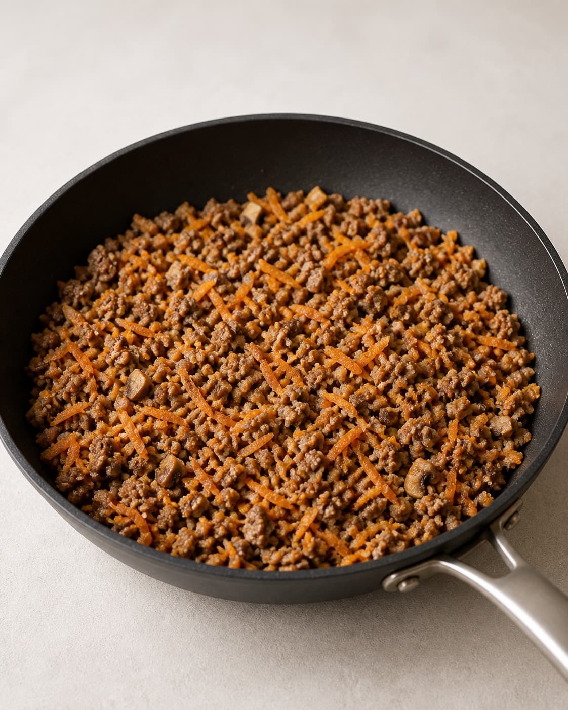 One skillet holding fully cooked crumbly pork filling with mushrooms and orange grated carrot, no noodles wrappers frying oil or finished rolls under tilberedningen af sprøde forårsruller