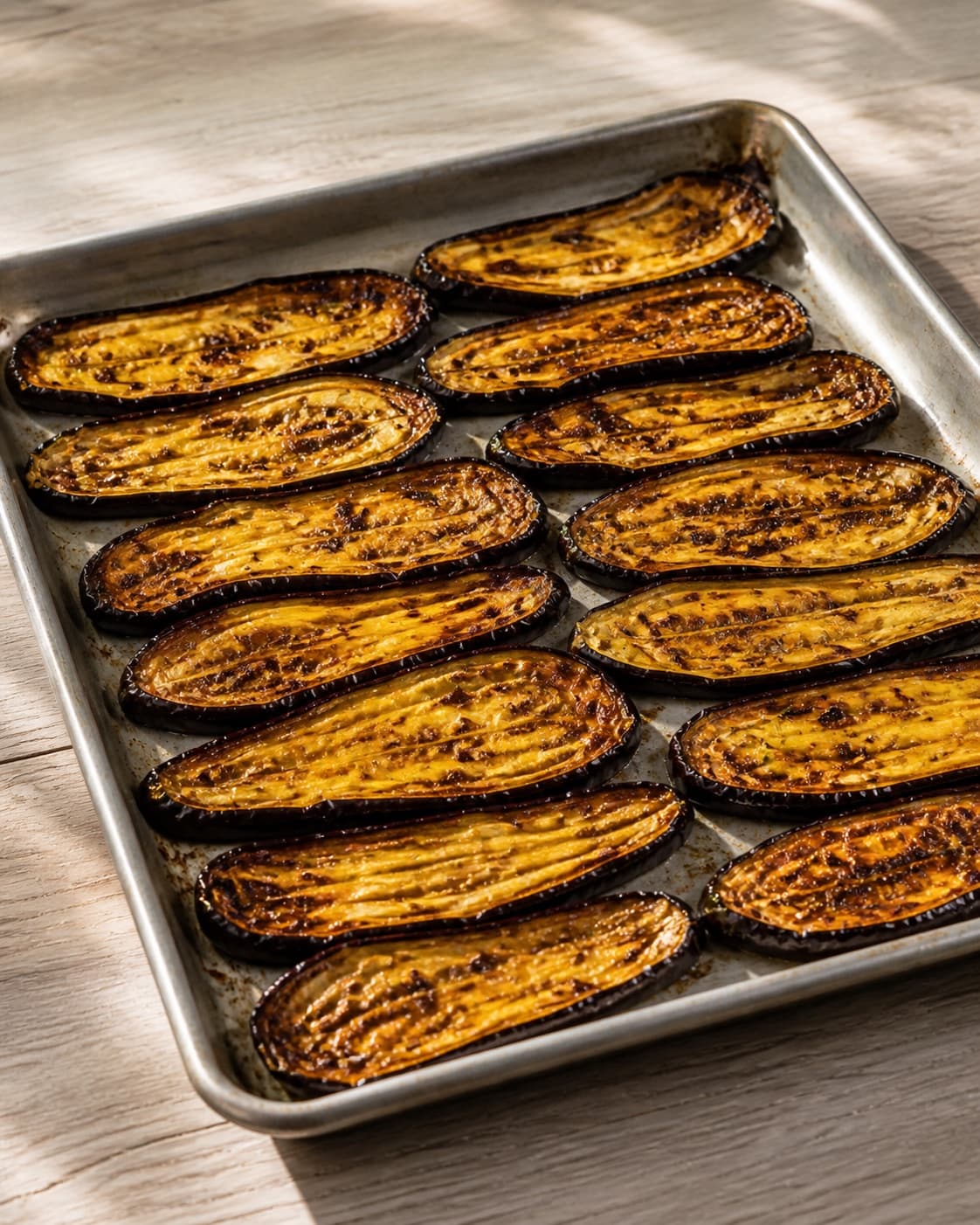 One baking tray holding tender collapsed golden-brown roasted aubergine slices, no dressing pistachios pomegranate mint or extra food under tilberedningen af grillet aubergine med tahindressing og mynte
