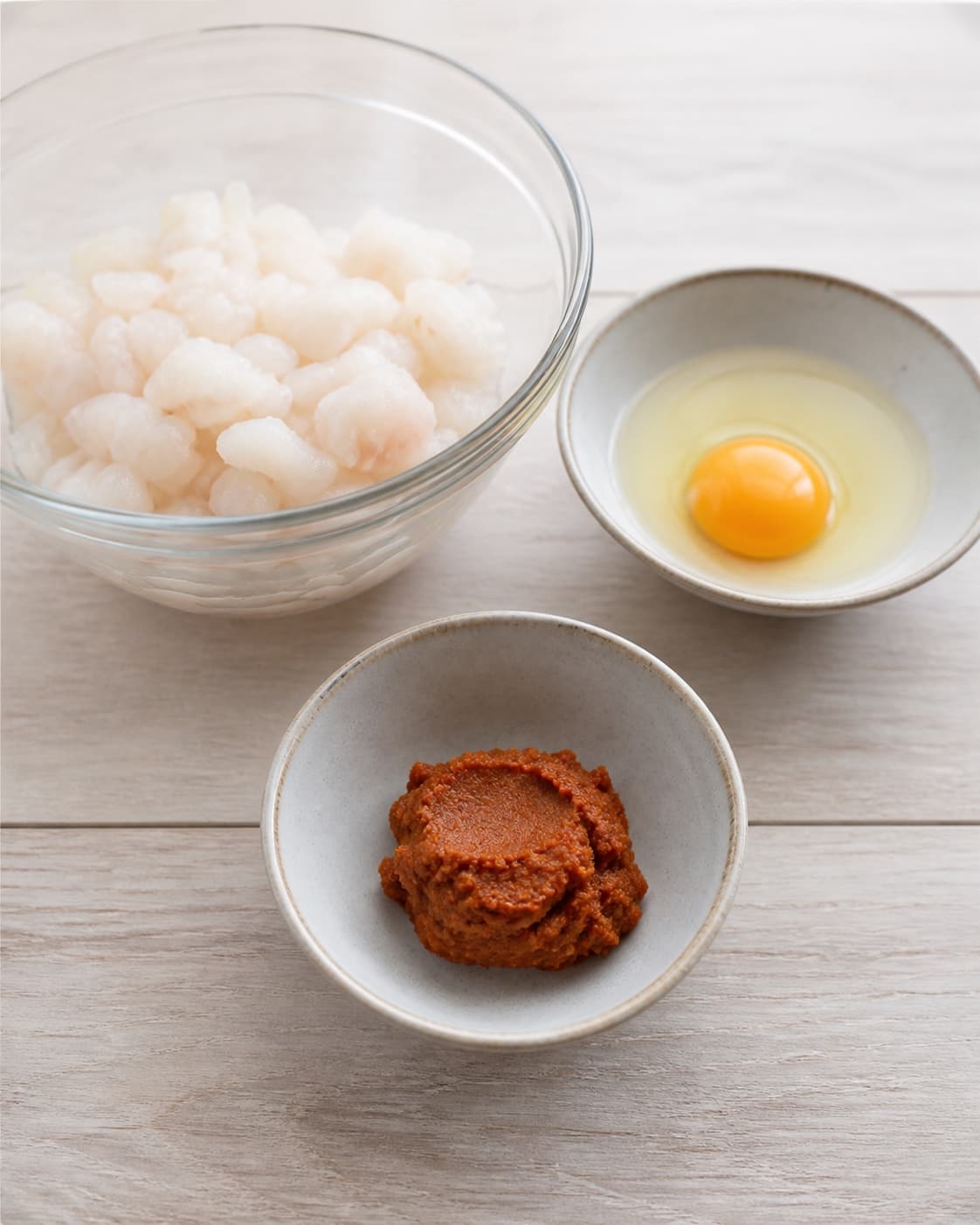 One single photorealistic instructional frame of finely prepared patty ingredients in separate bowls for Thai fiskefrikadeller, featuring torskefilet, rød karrypasta, æg, with only the named equipment and no unrelated food, text, logos or packaging under tilberedningen af thai fiskefrikadeller