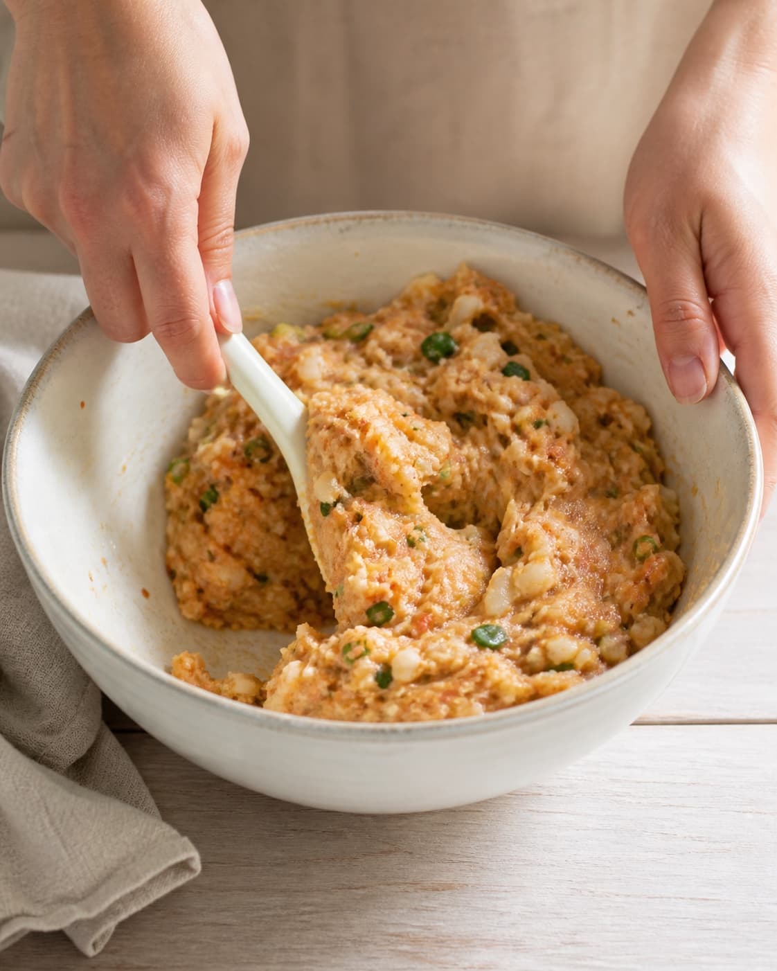 One single photorealistic instructional frame of the cohesive patty mixture being folded in one bowl for Thai fiskefrikadeller, featuring torskefilet, rød karrypasta, æg, with only the named equipment and no unrelated food, text, logos or packaging under tilberedningen af thai fiskefrikadeller