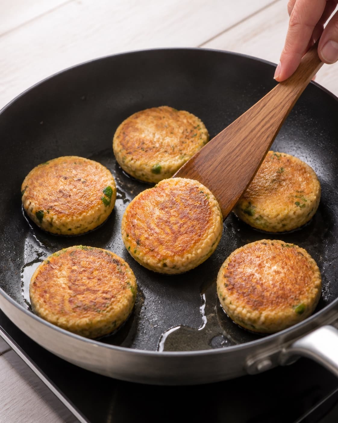 One single photorealistic instructional frame of equal patties browning in one skillet for Thai fiskefrikadeller, featuring torskefilet, rød karrypasta, æg, with only the named equipment and no unrelated food, text, logos or packaging under tilberedningen af thai fiskefrikadeller
