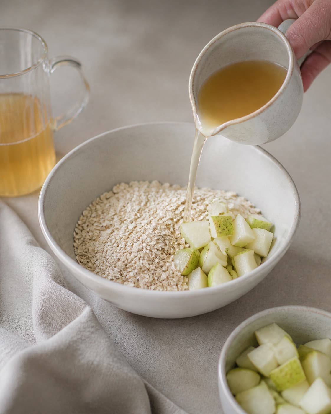 One single photorealistic instructional frame of measured grains seeds and liquid before cooking for Bircher Müsli med pære, featuring grove havregryn, pære, æblejuice, with only the named equipment and no unrelated food, text, logos or packaging under tilberedningen af bircher müsli med pære