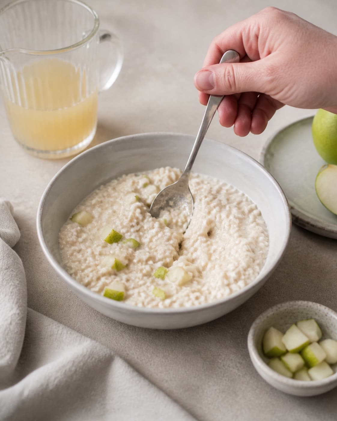One single photorealistic instructional frame of the porridge consistency being adjusted with a spoon for Bircher Müsli med pære, featuring grove havregryn, pære, æblejuice, with only the named equipment and no unrelated food, text, logos or packaging under tilberedningen af bircher müsli med pære