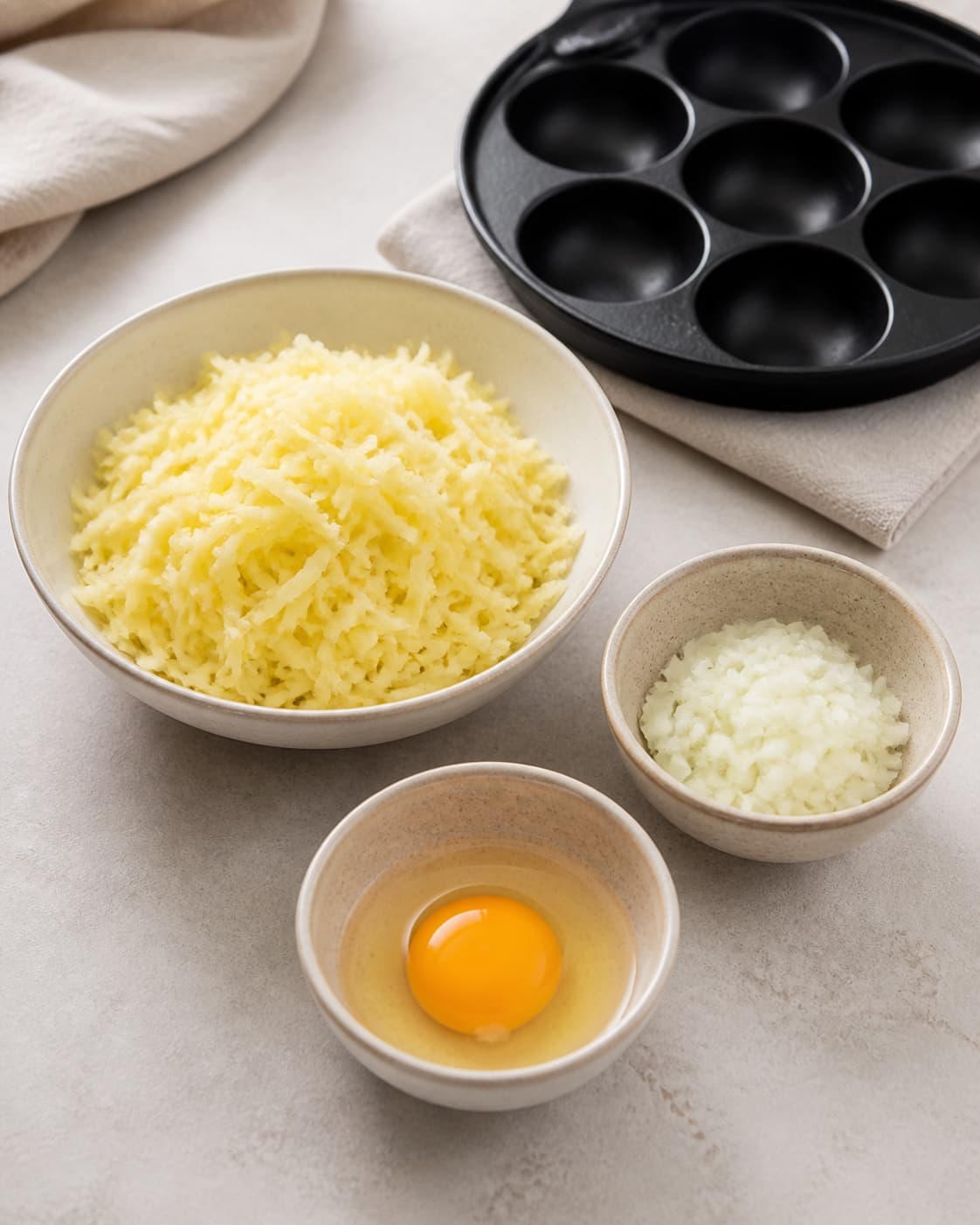 One single photorealistic instructional frame of finely prepared patty ingredients in separate bowls for Rösti - lavet i æbleskivepanden, featuring kartofler, løg, æg, with only the named equipment and no unrelated food, text, logos or packaging under tilberedningen af rösti - lavet i æbleskivepanden